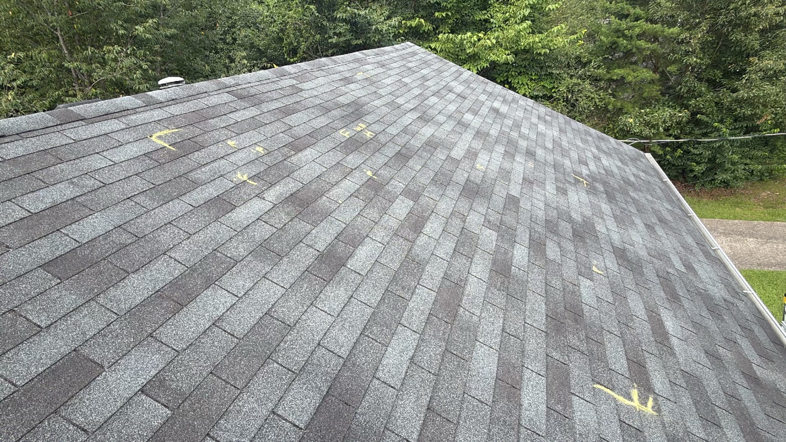 Yellow chalk marks from an insurance adjuster circling hail hits across an asphalt shingle roof