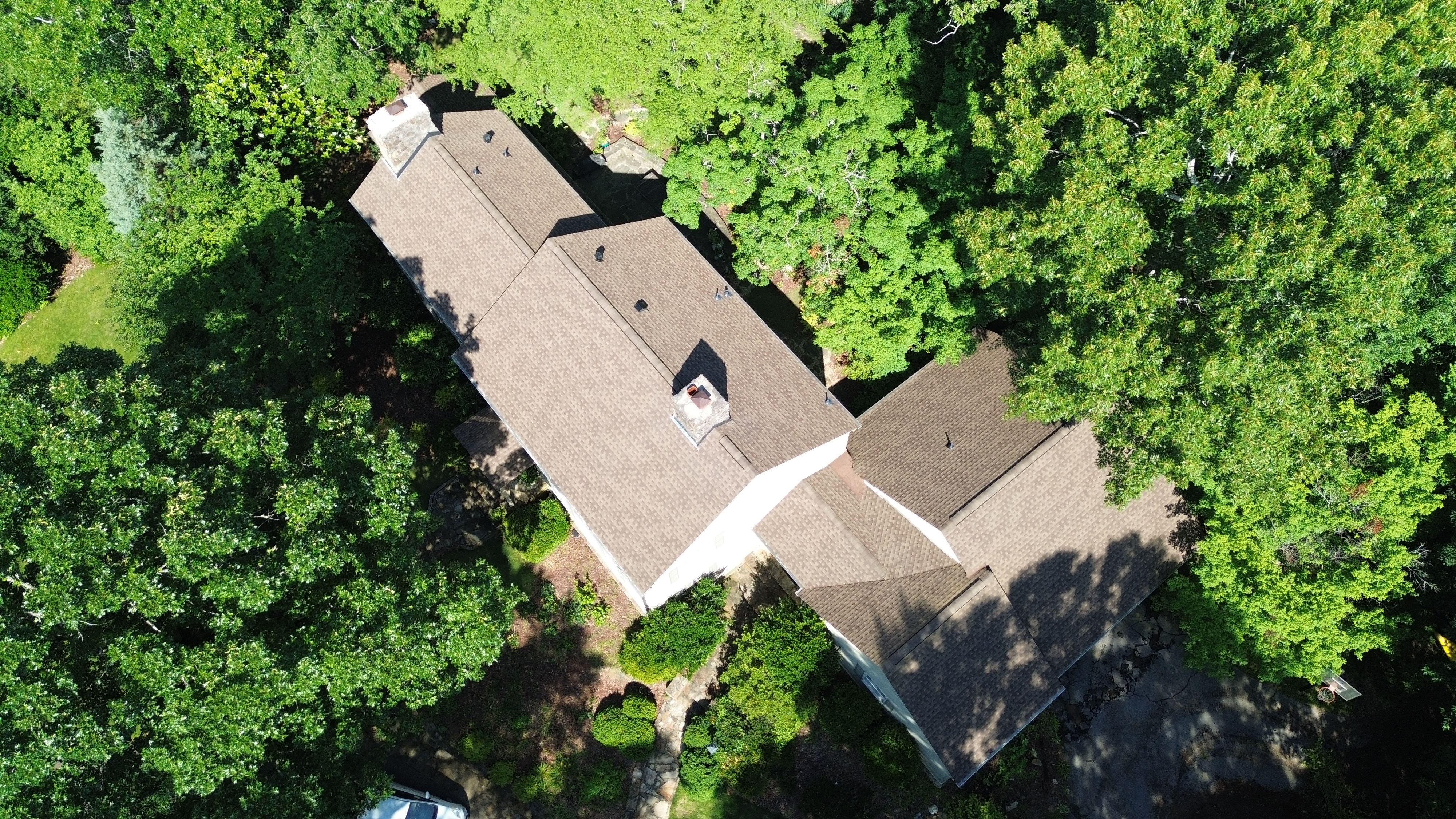 Lush green trees surround a completed brown shingle roof replacement along Old Leeds Road.