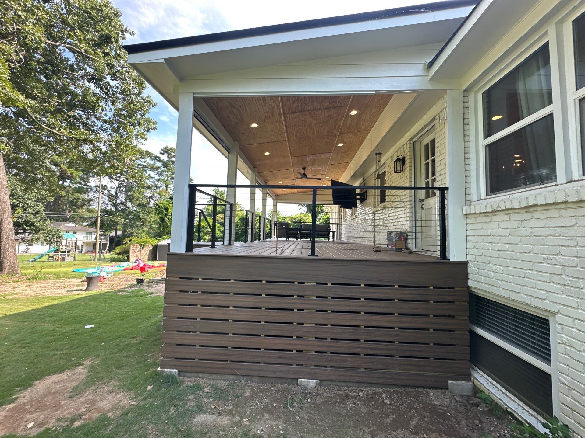 Side view of a modern screened-in deck featuring a wood-paneled ceiling, fan, and sleek black railings in Vestavia Hills.