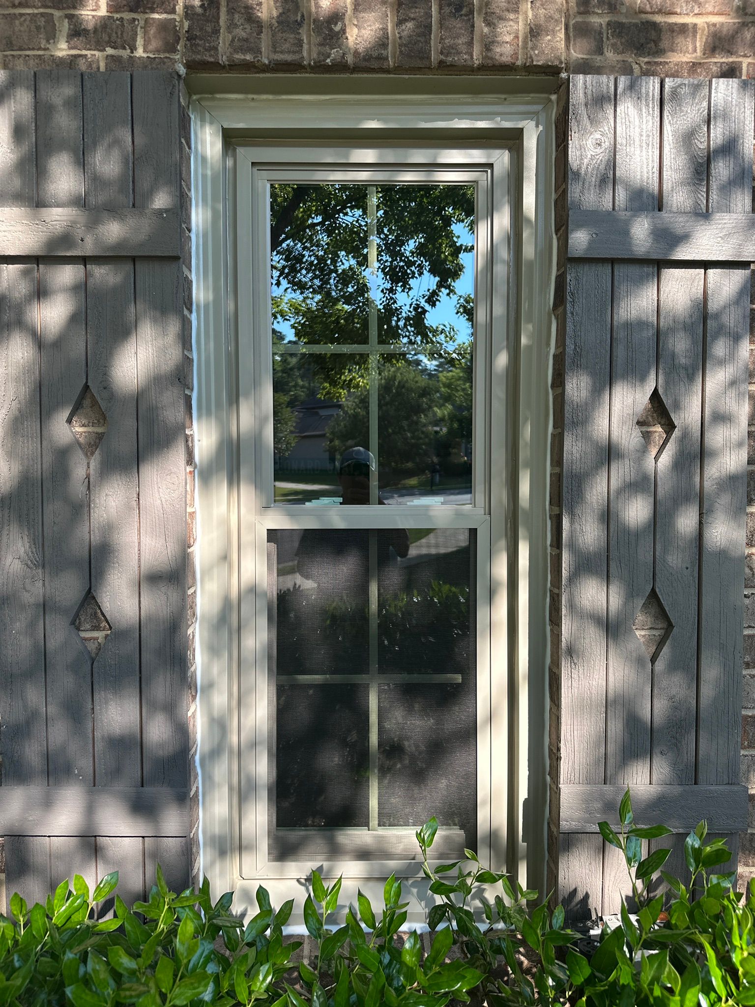A newly installed window replacement framed by wooden shutters on a brick home in the Bluff Park neighborhood.