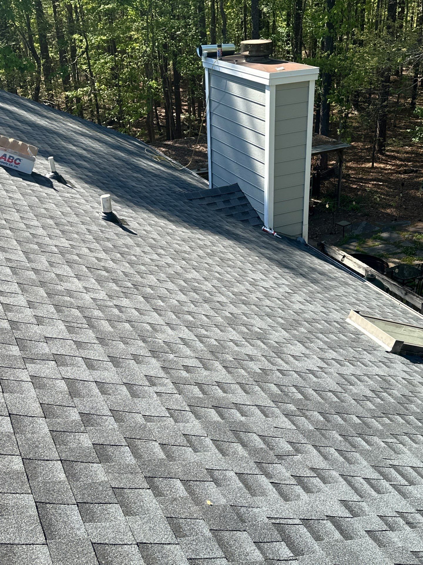 A newly installed gray asphalt shingle roof on a home in Chelsea featuring a chimney and roof vents.