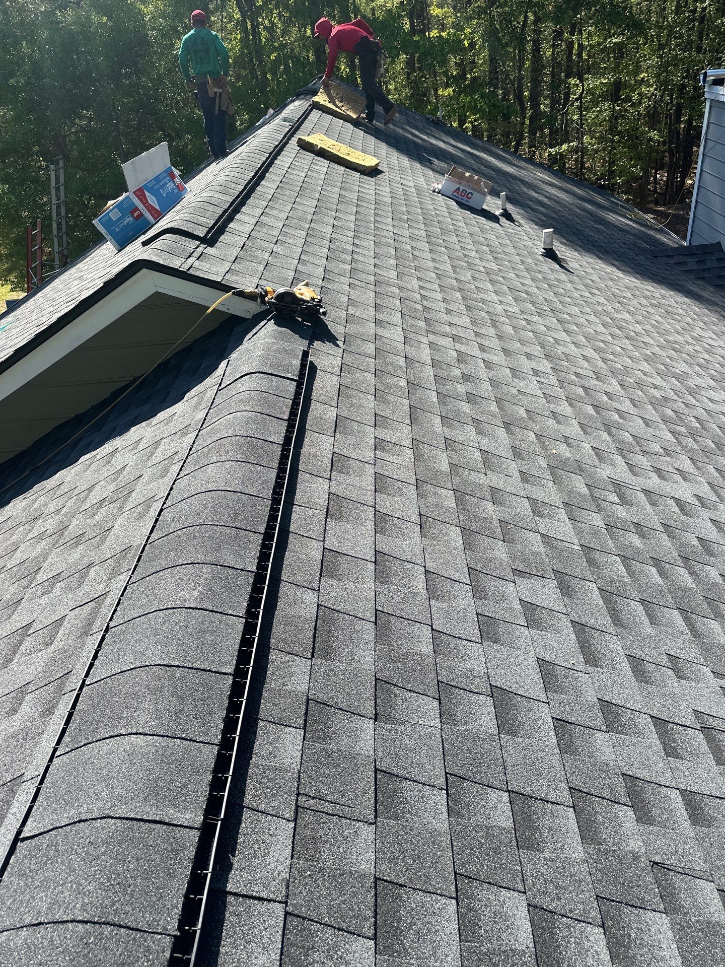 Workers installing new dark architectural shingles during a roof replacement in Chelsea.