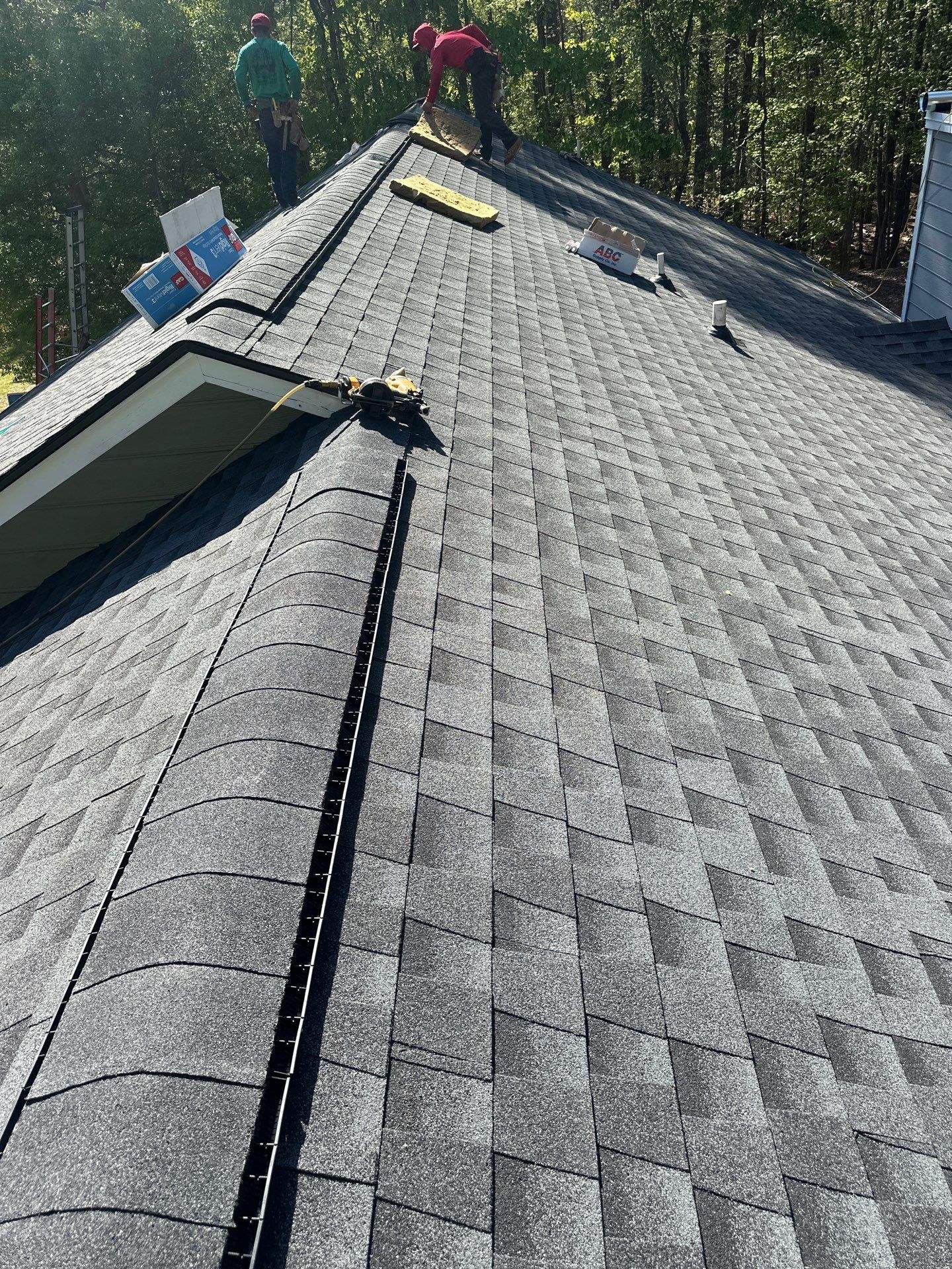 Workers installing new dark architectural shingles during a roof replacement in Chelsea.