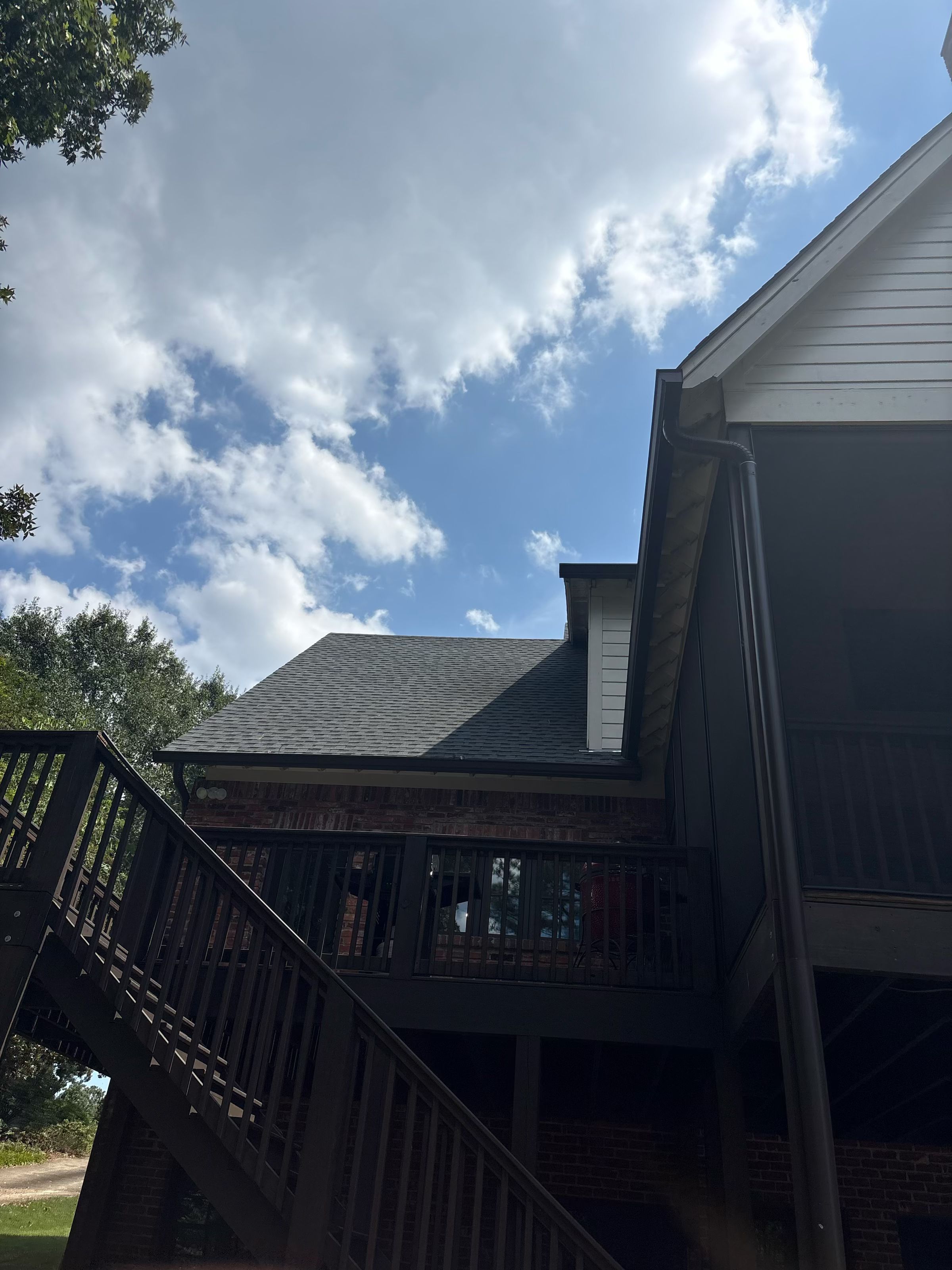Looking up at newly protected gutters along a shingle roof plane above a dark backyard deck.