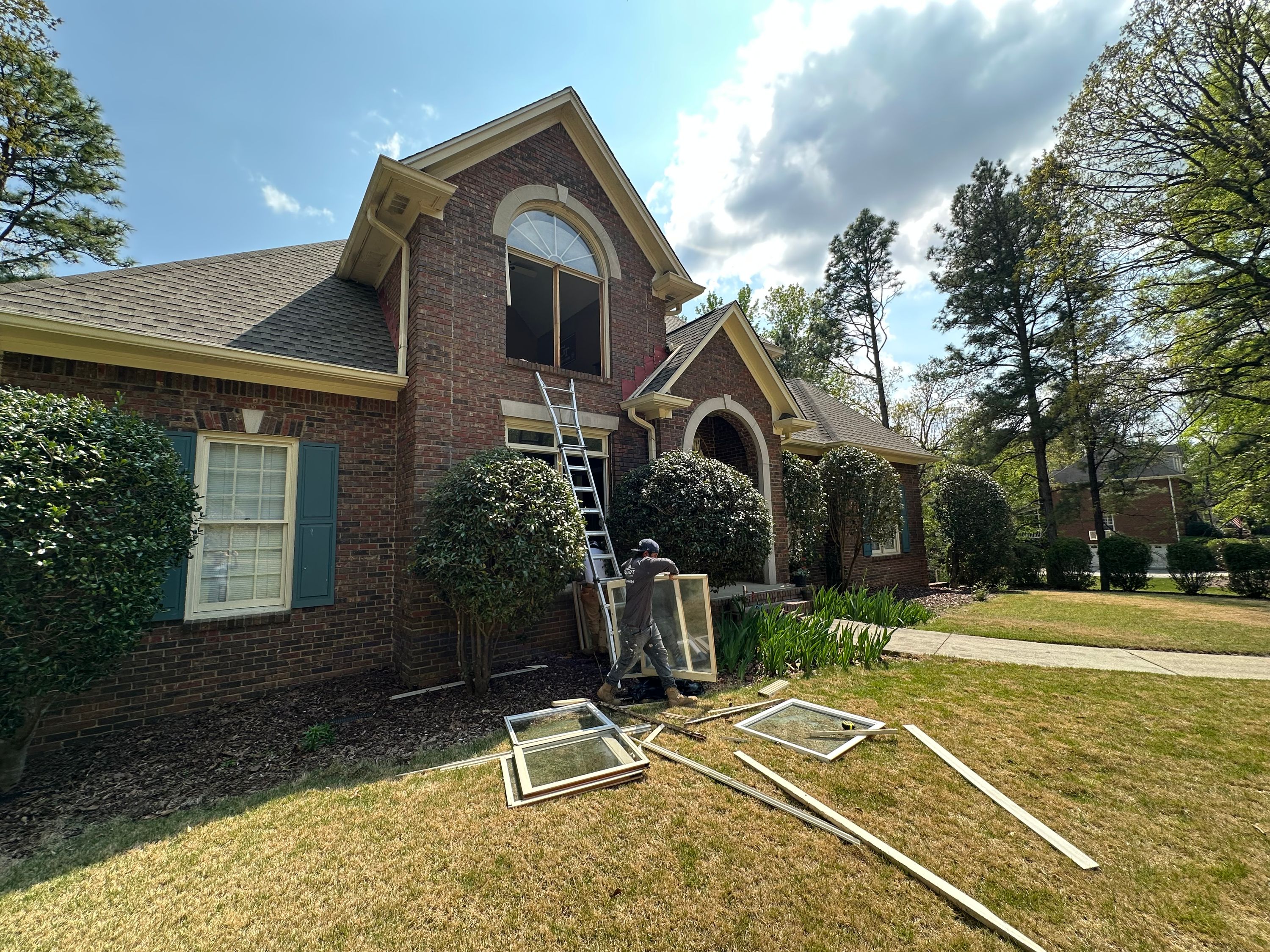 A Patriot crew member carries a removed window sash near an extension ladder for a Hoover window replacement.