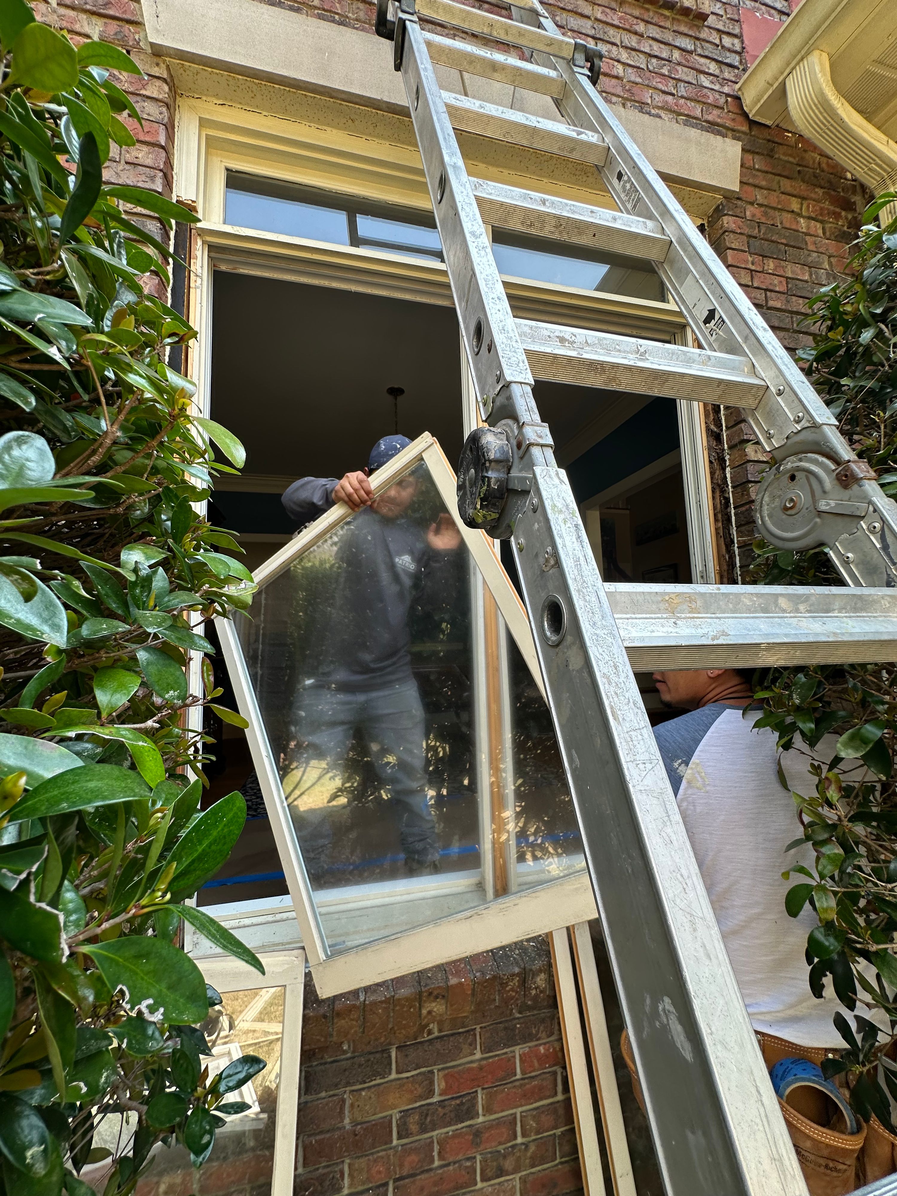 Patriot workers remove a window sash next to an extension ladder for a Hoover window replacement.