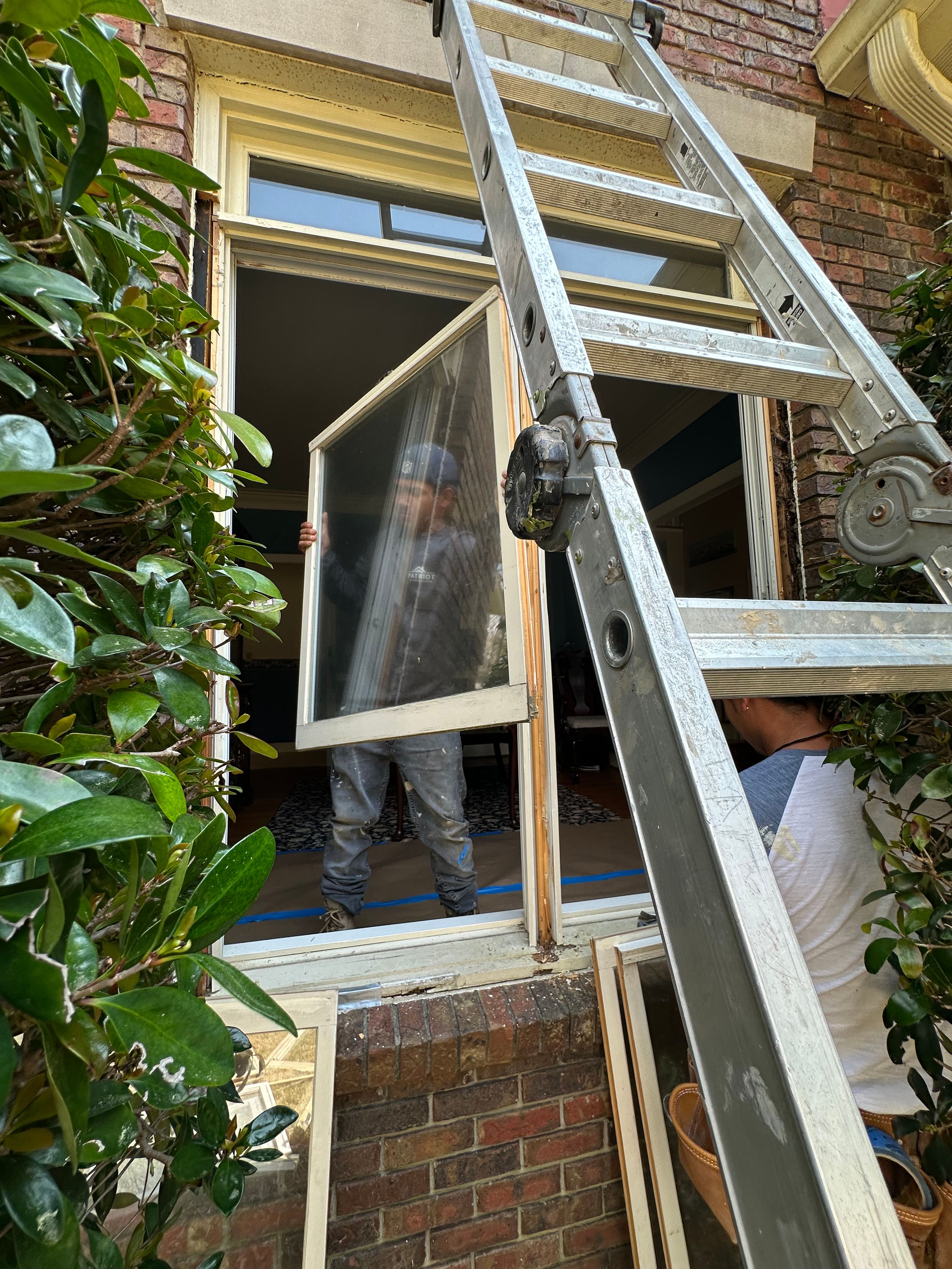 Patriot Roofing and Builders replace a window sash near an extension ladder at a brick home in Hoover.