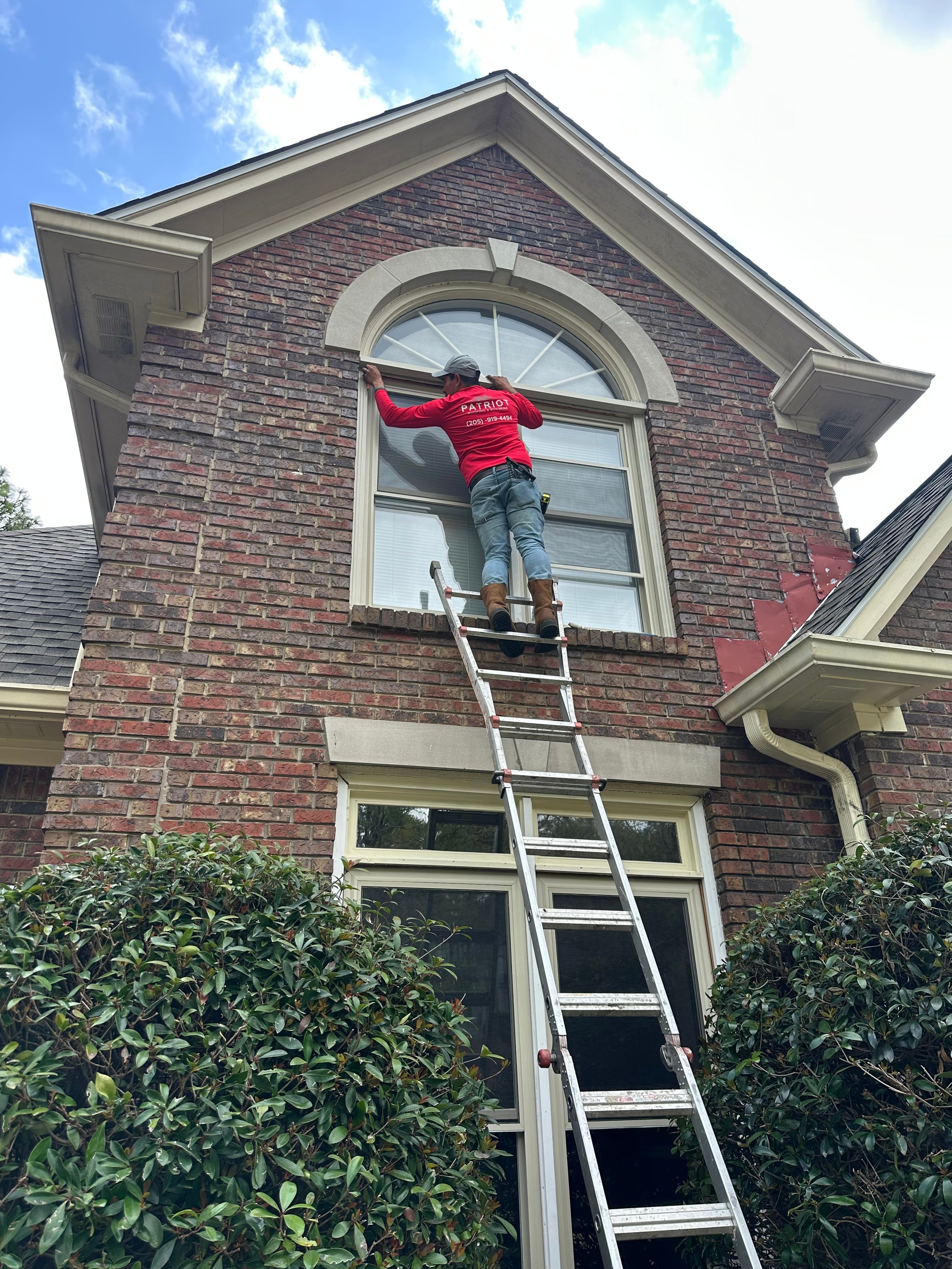 A Patriot installer measures an arched second-story window for replacement from an extension ladder in Hoover.