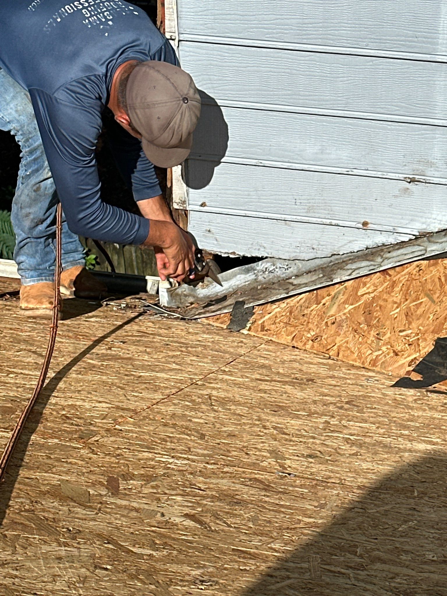 Cutting metal flashing on OSB decking during a roof replacement in Helena.