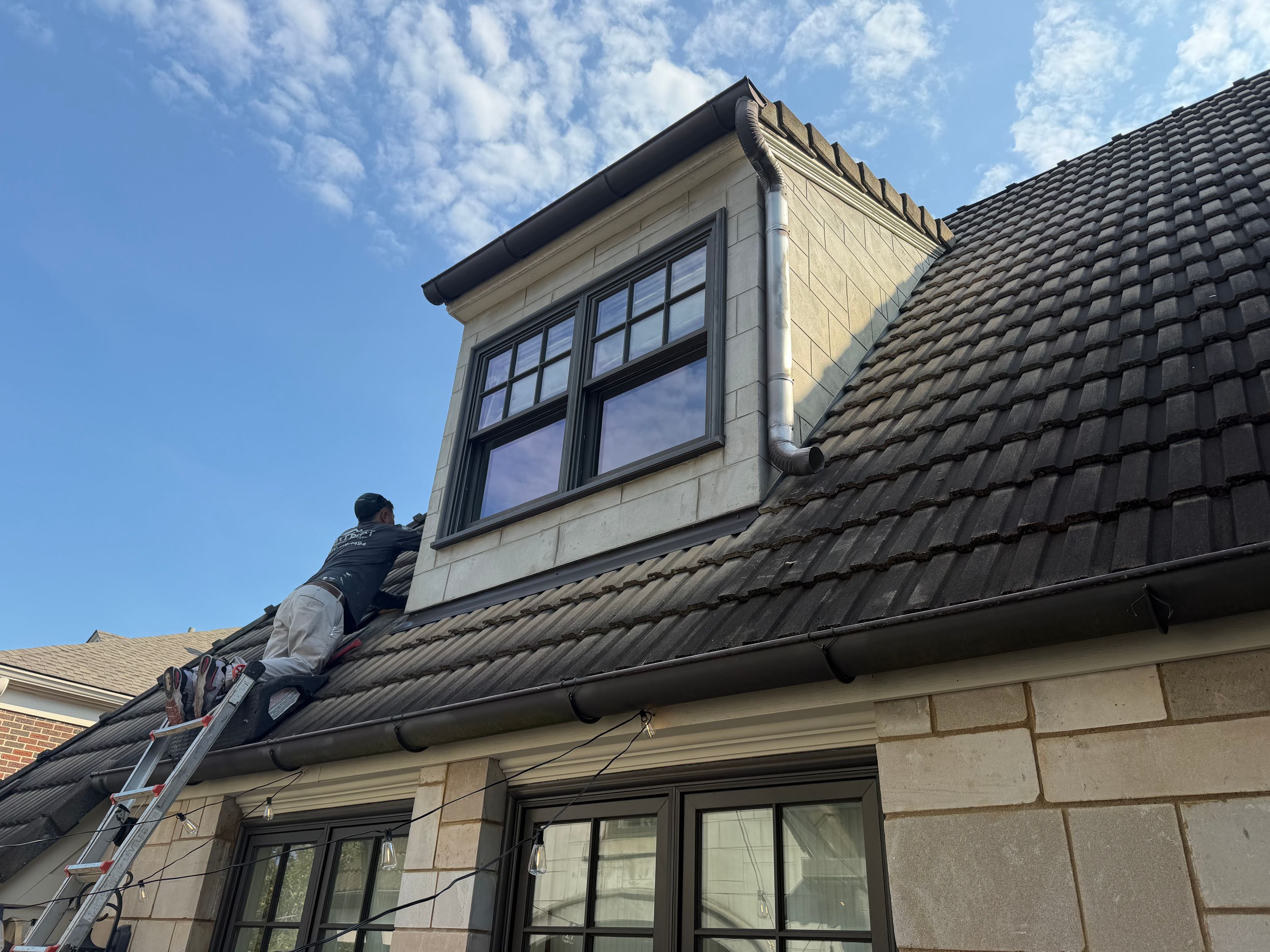 Metal wall flashing and gutters line dark roof tiles near windows on a Birmingham home.