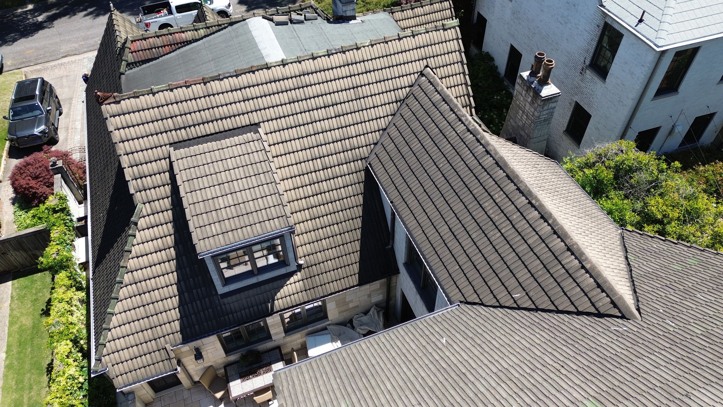 Intersecting tile roof slopes and dormer windows viewed from above during a roof repair project.