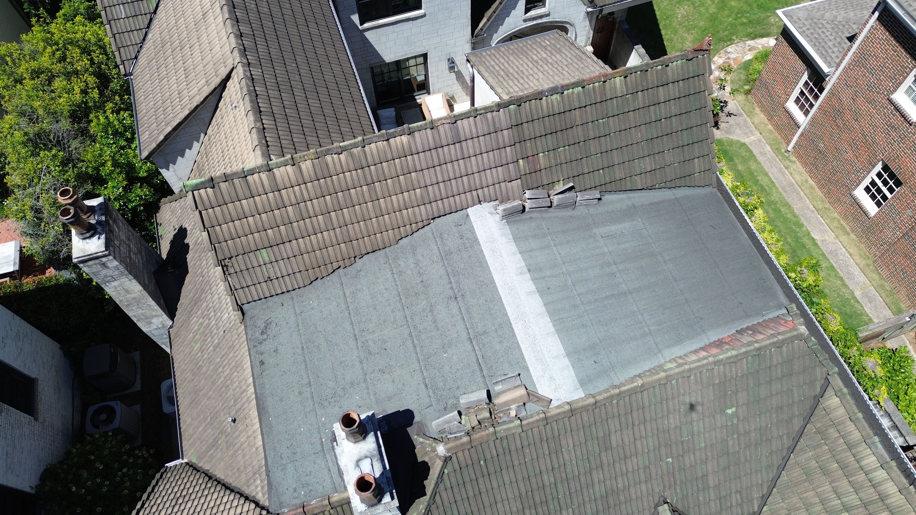 A flat membrane section meets concrete tiles and dual chimney flues on a home in Forest Park.