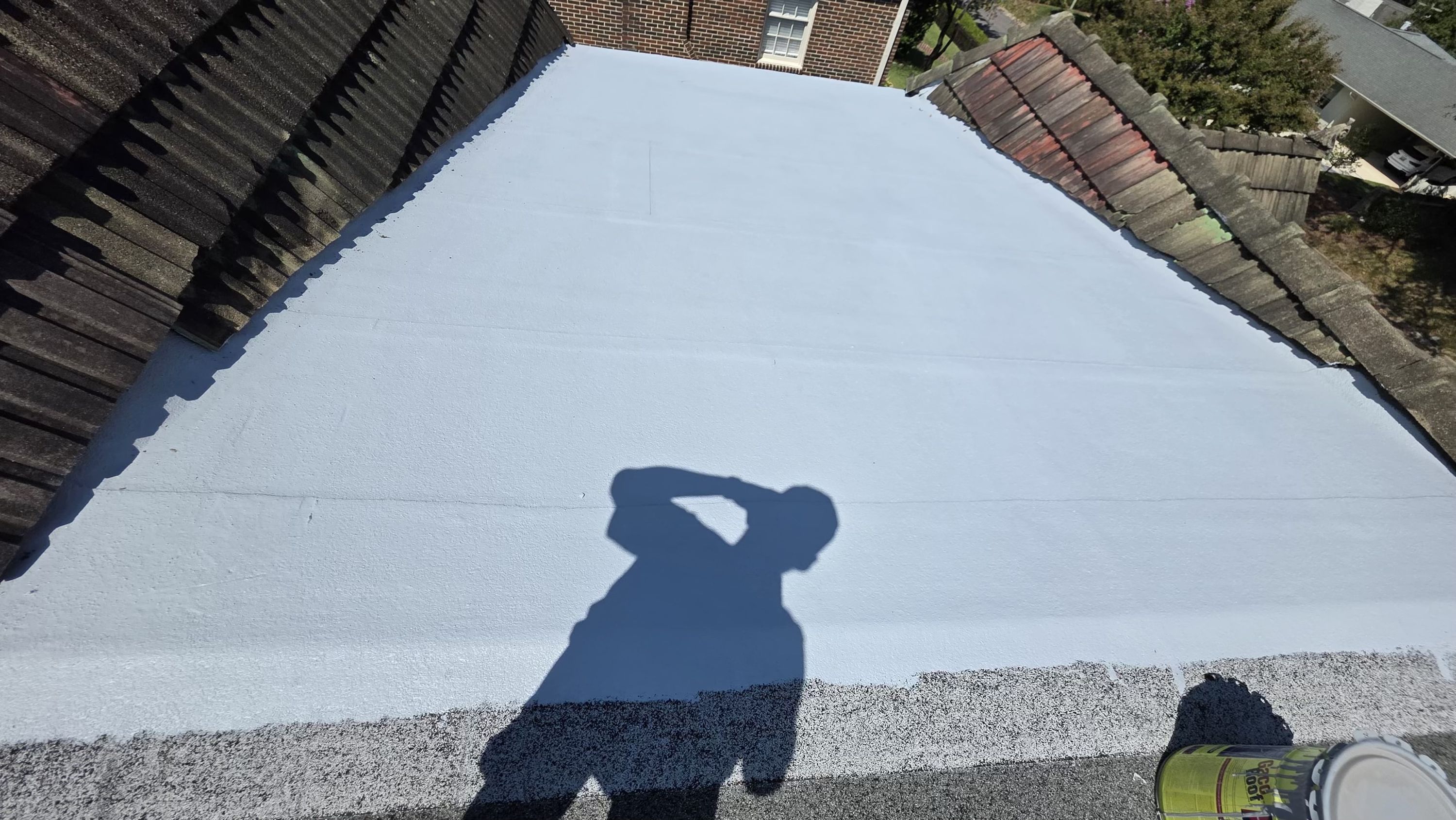 Freshly coated flat roof section transitioning to dark granule membrane beside a brick exterior.