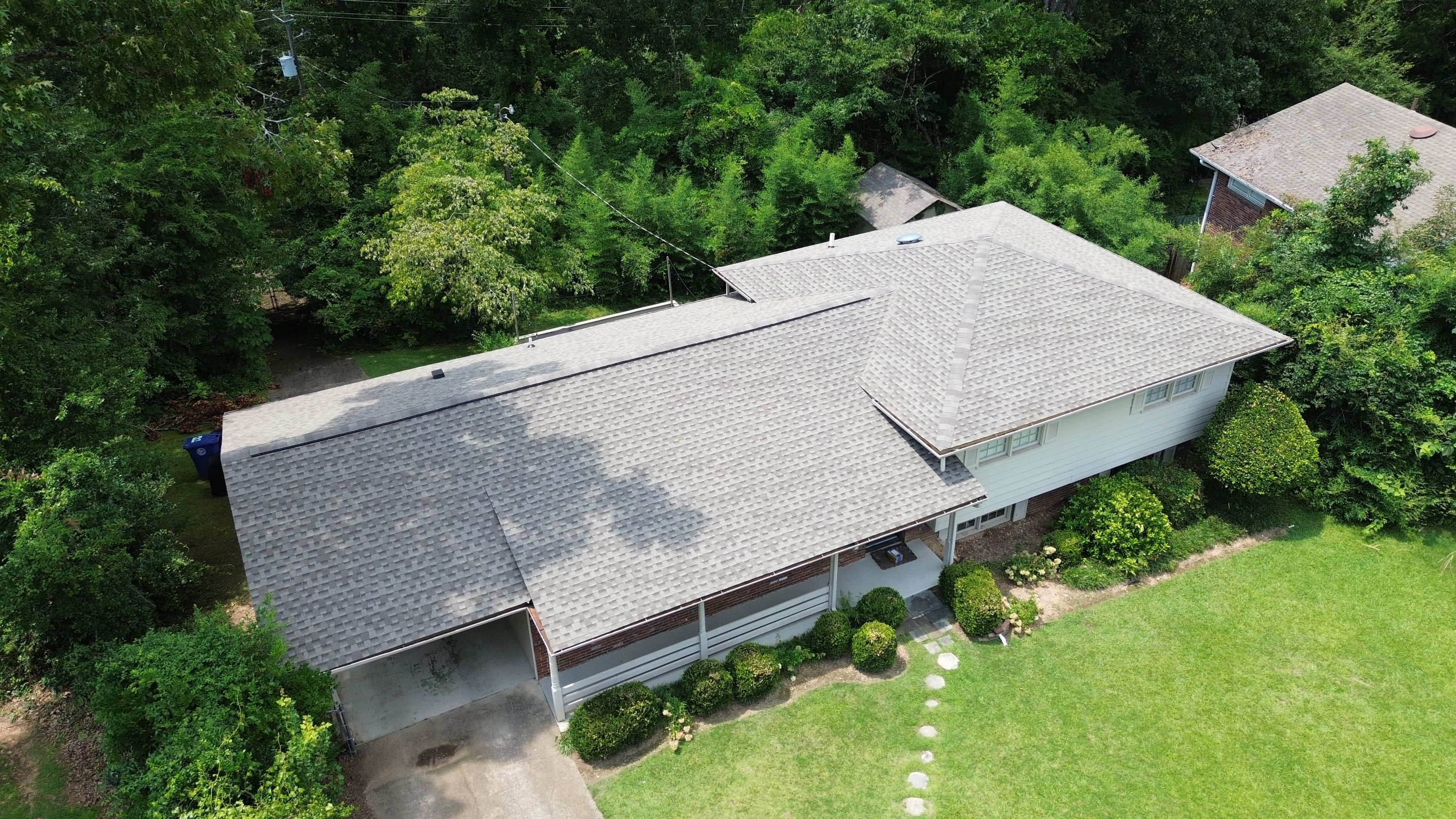 Looking down on completed grey shingling and ridge caps on a residential roof replacement.