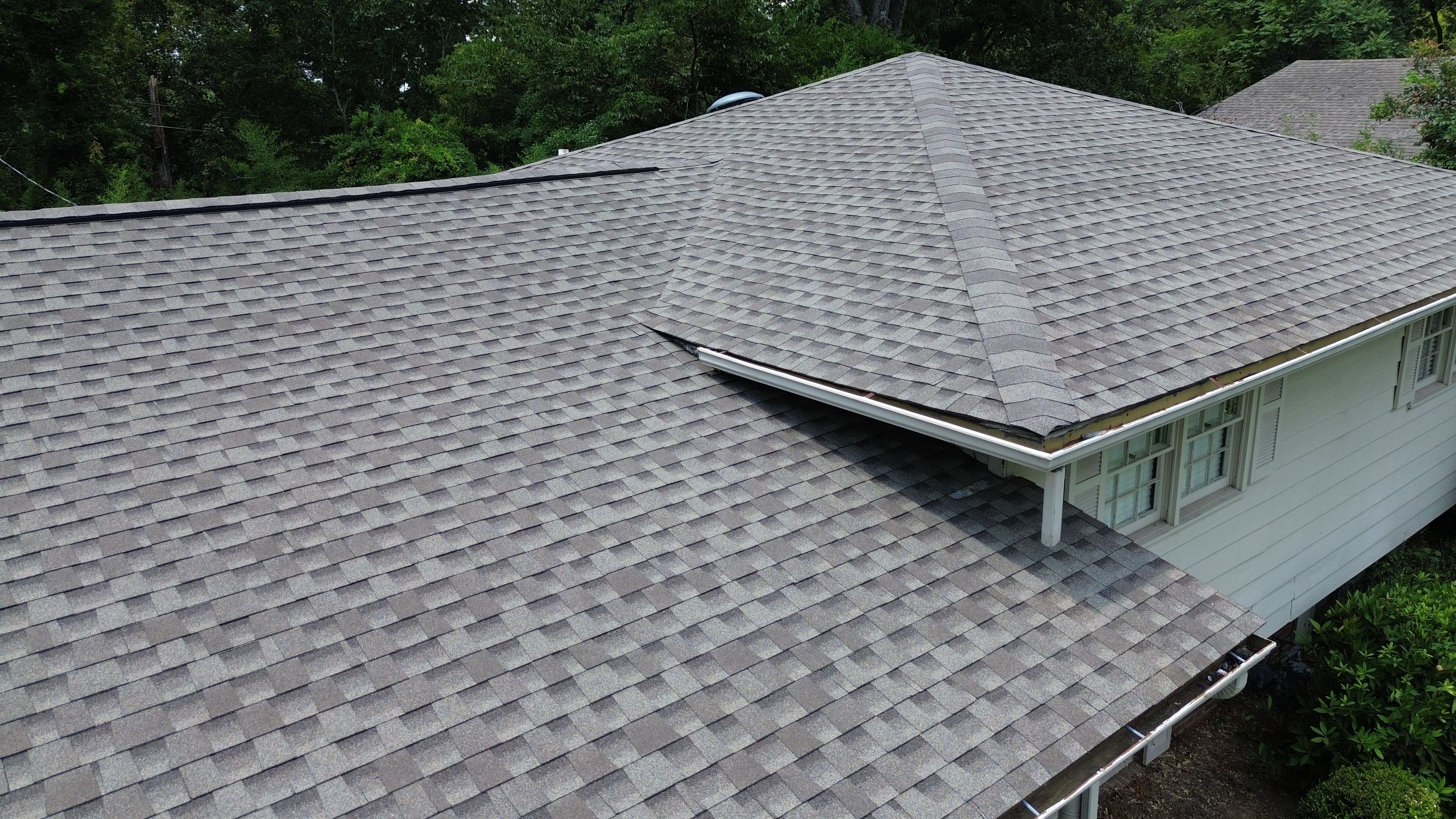 A clean white gutter run sits nestled in the valley of a newly completed shingle roof replacement.