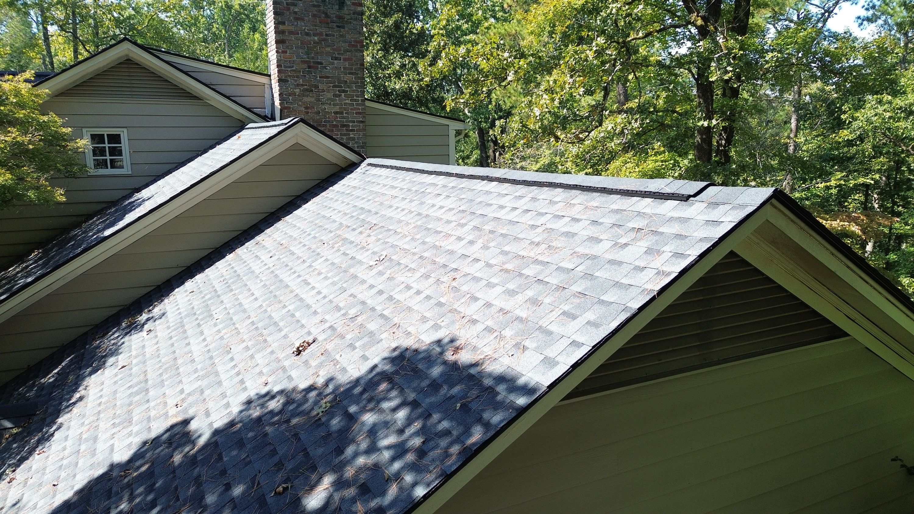 Newly installed grey asphalt shingles along a roof plane near a brick chimney on a Mountain Brook home.