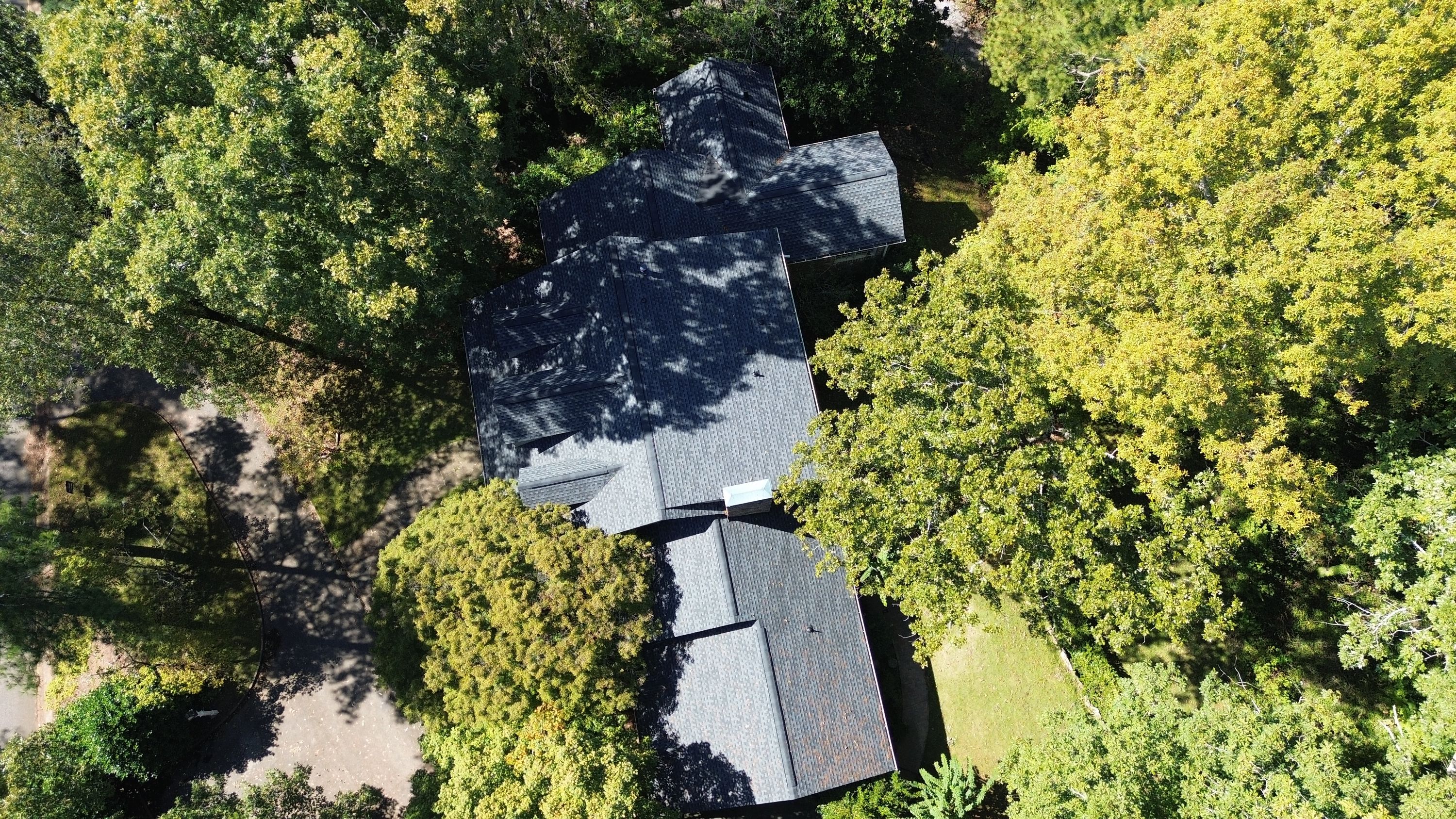 Aerial perspective of a completed multi-gabled shingle roof replacement surrounded by trees in Mountain Brook.