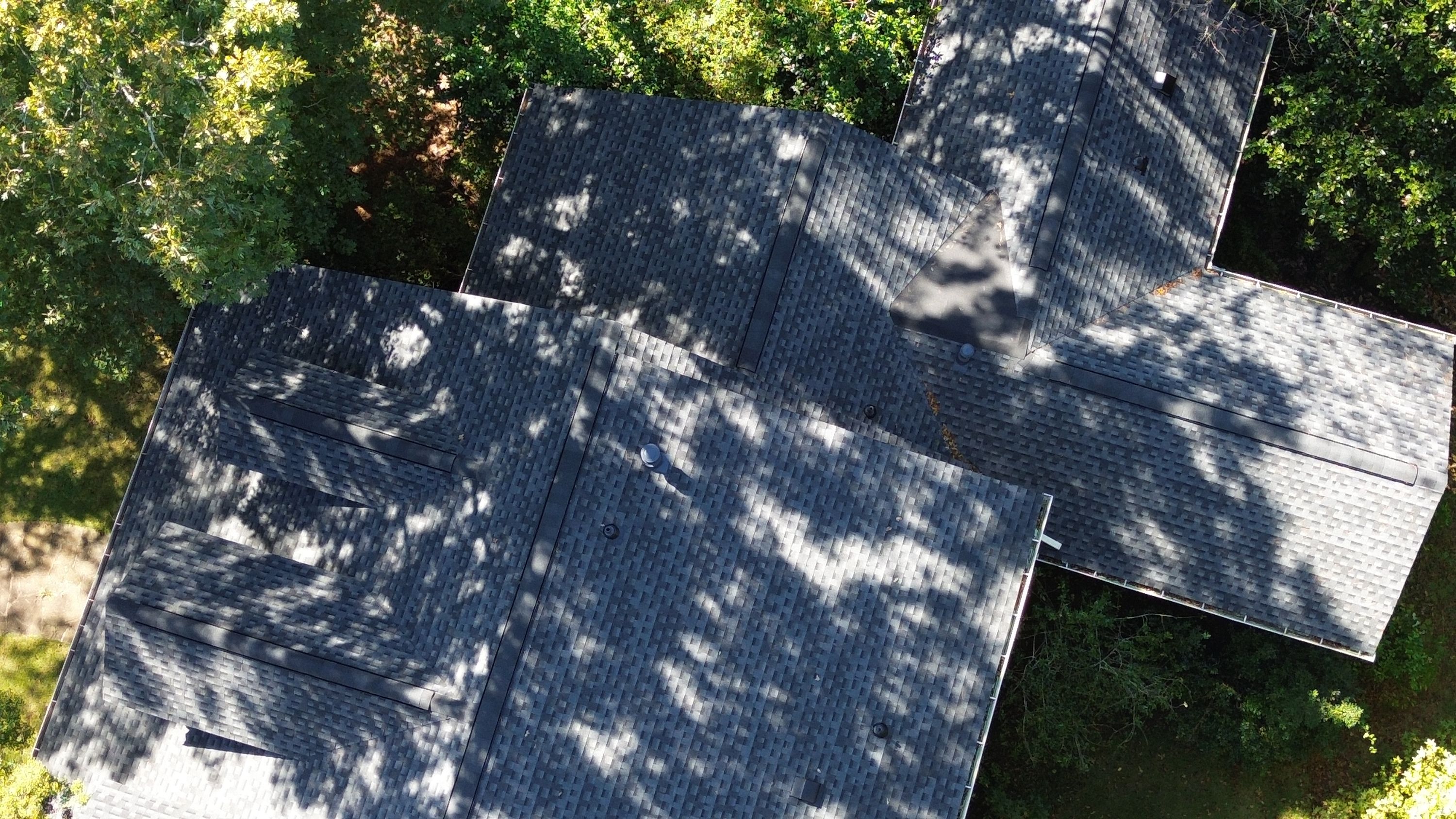 Top-down detail of grey architectural shingles installed around pipe vent boots and roof vents.