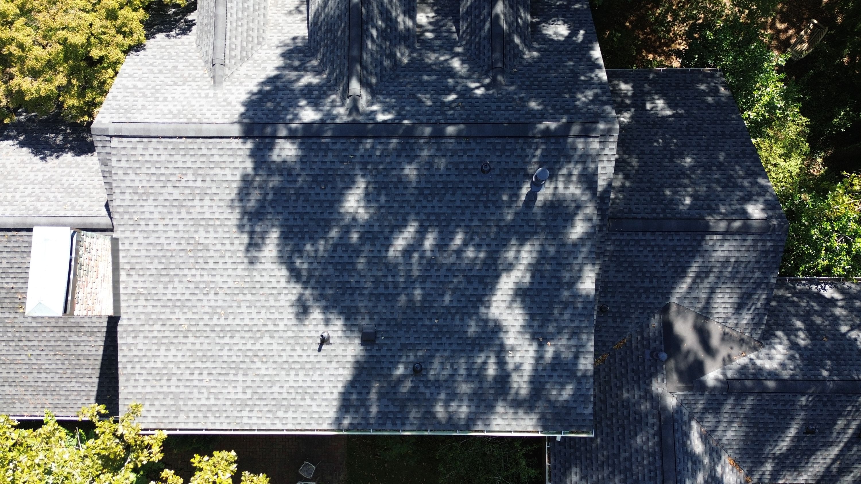 Direct overhead view showing clean ridge cap installation and roof penetrations on dark grey shingles.