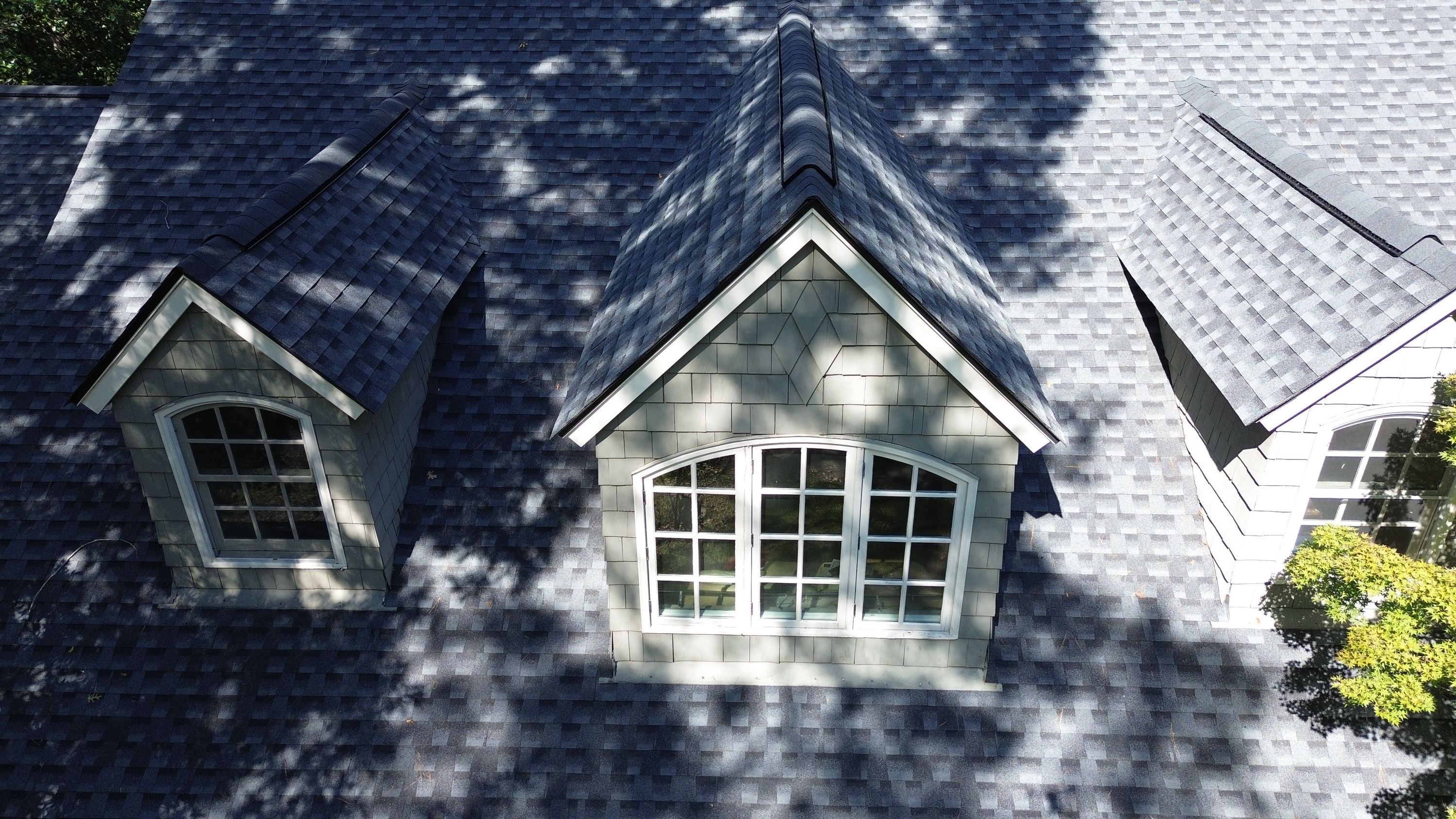 High-angle view of a dormer roof peak showing newly installed grey asphalt shingles and ridge cap.
