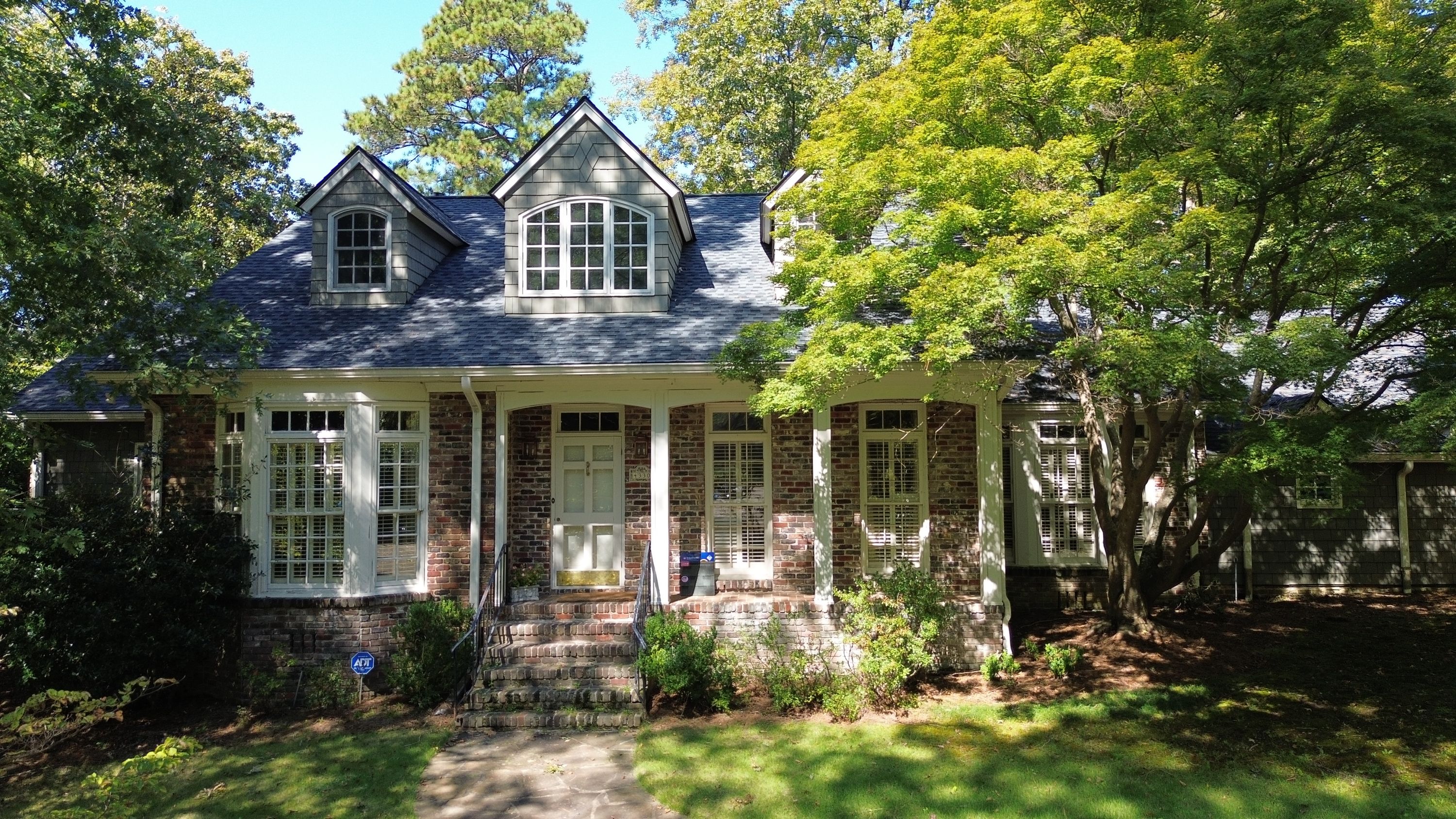 Ground-level perspective of a brick home with new shingle roofing on twin dormers above the front porch.