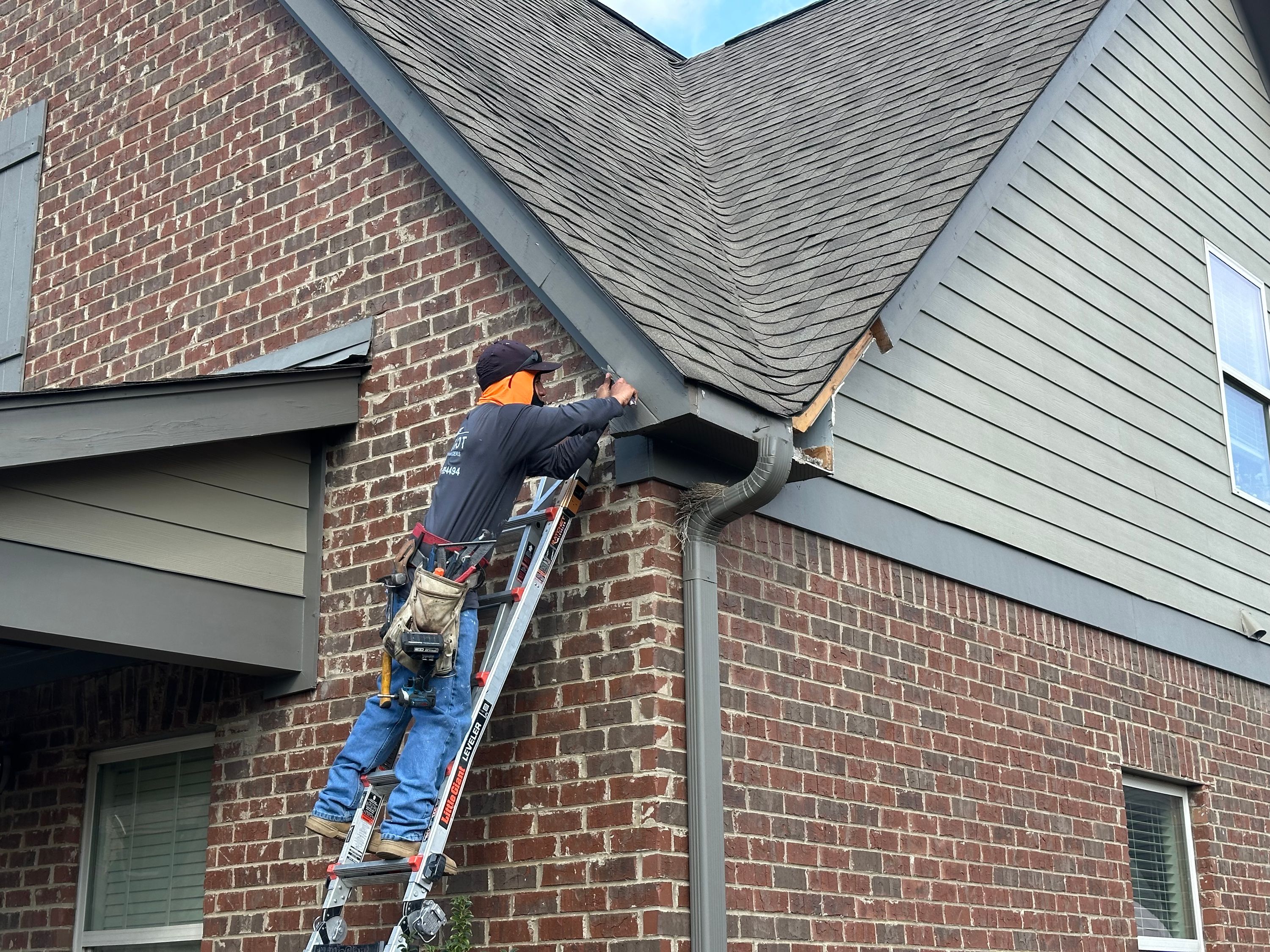 Contractor on a ladder performing roof repair on a brick home in Chelsea Park.