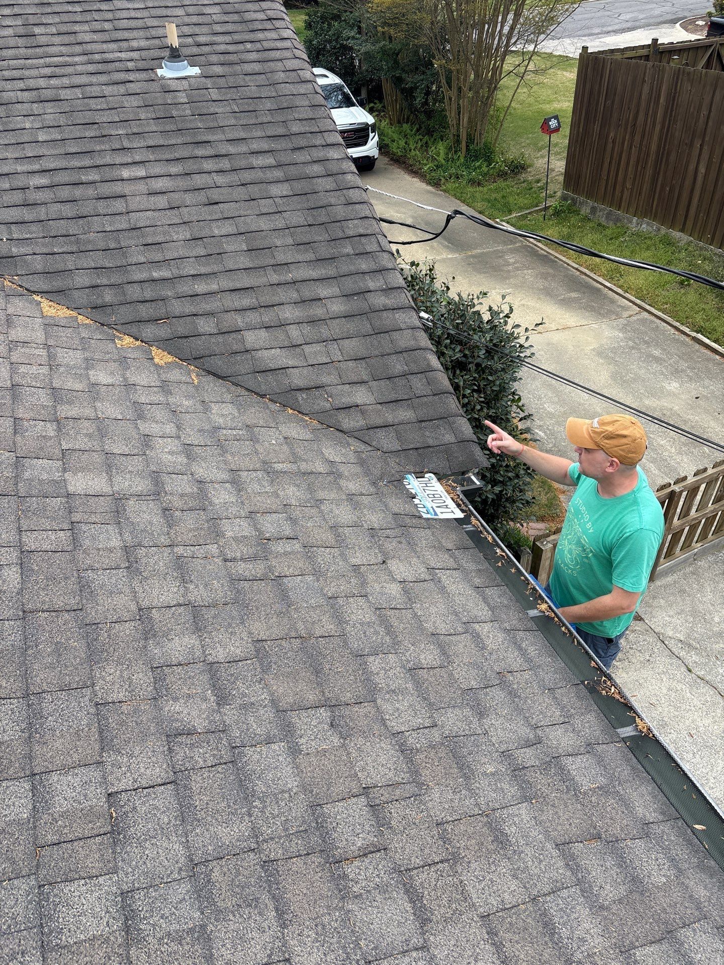 An overhead view of shingle roofing showing a license plate slipped under a valley before a roof repair.