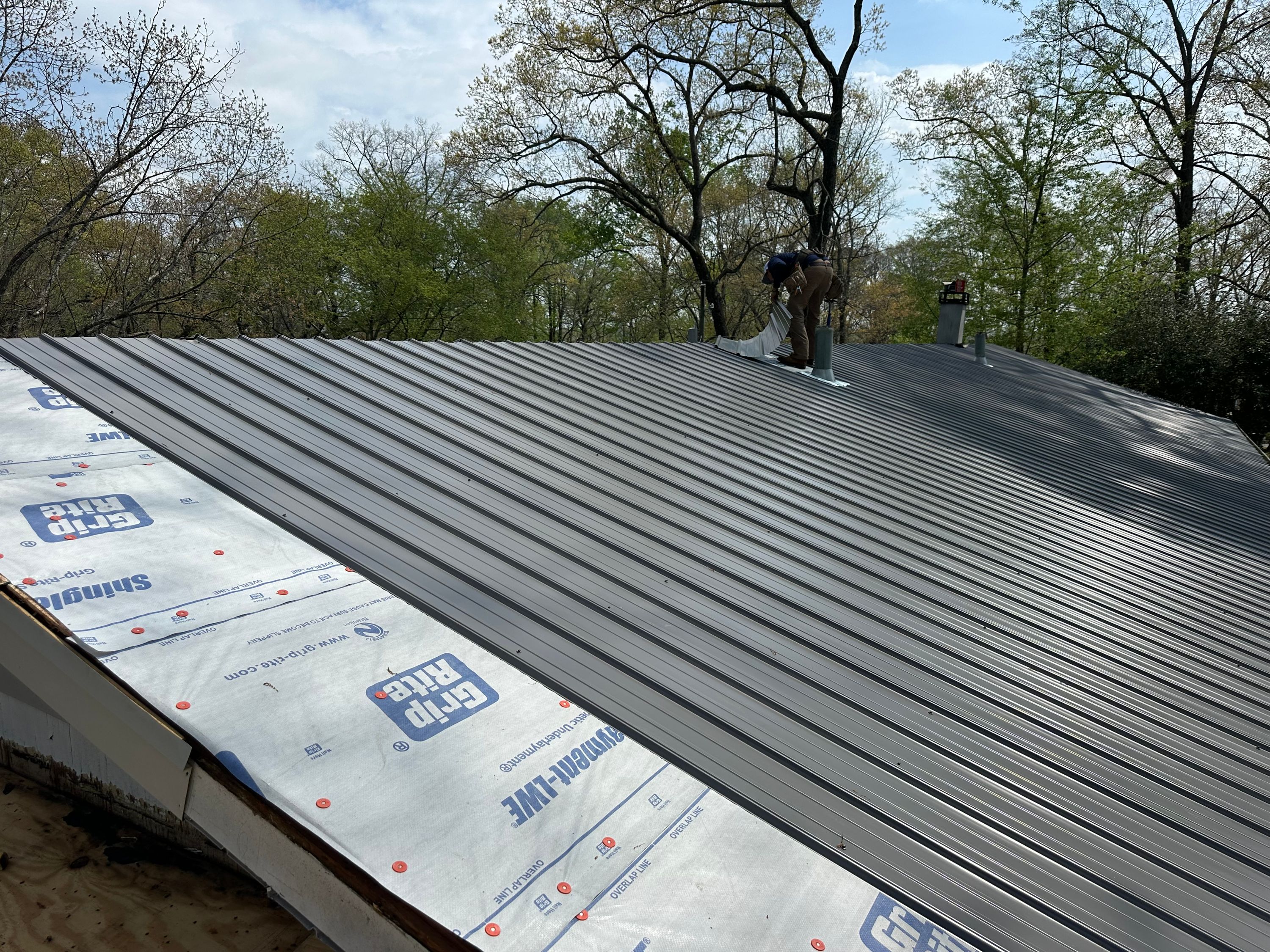 Metal roof replacement in Cahaba Heights showing gray panels being installed over protective underlayment.