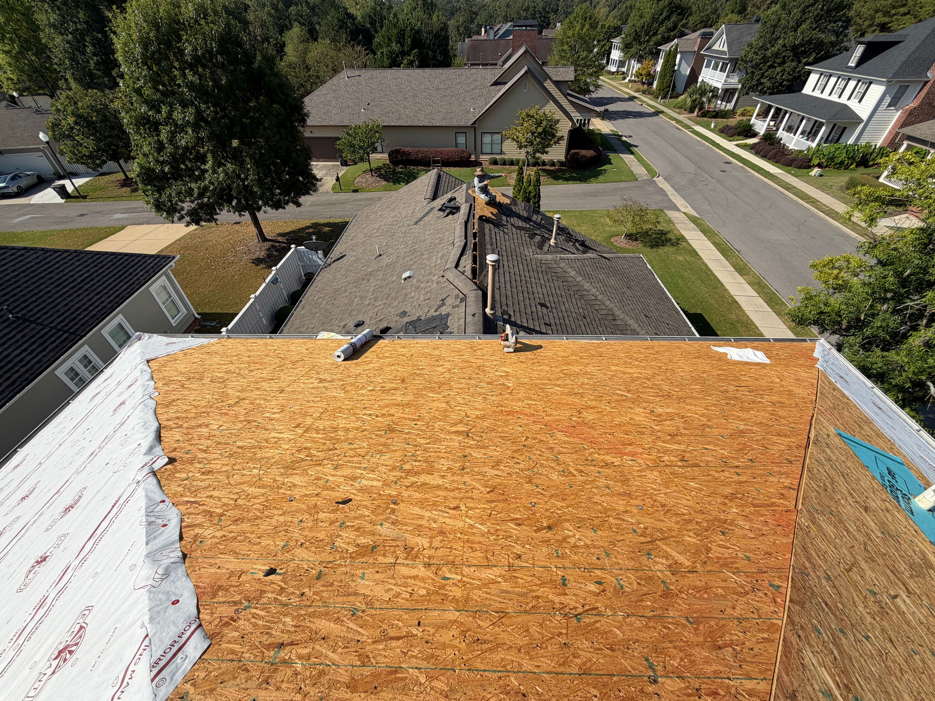 Foreground OSB roof decking transitions to older shingles during a Hoover roof replacement.