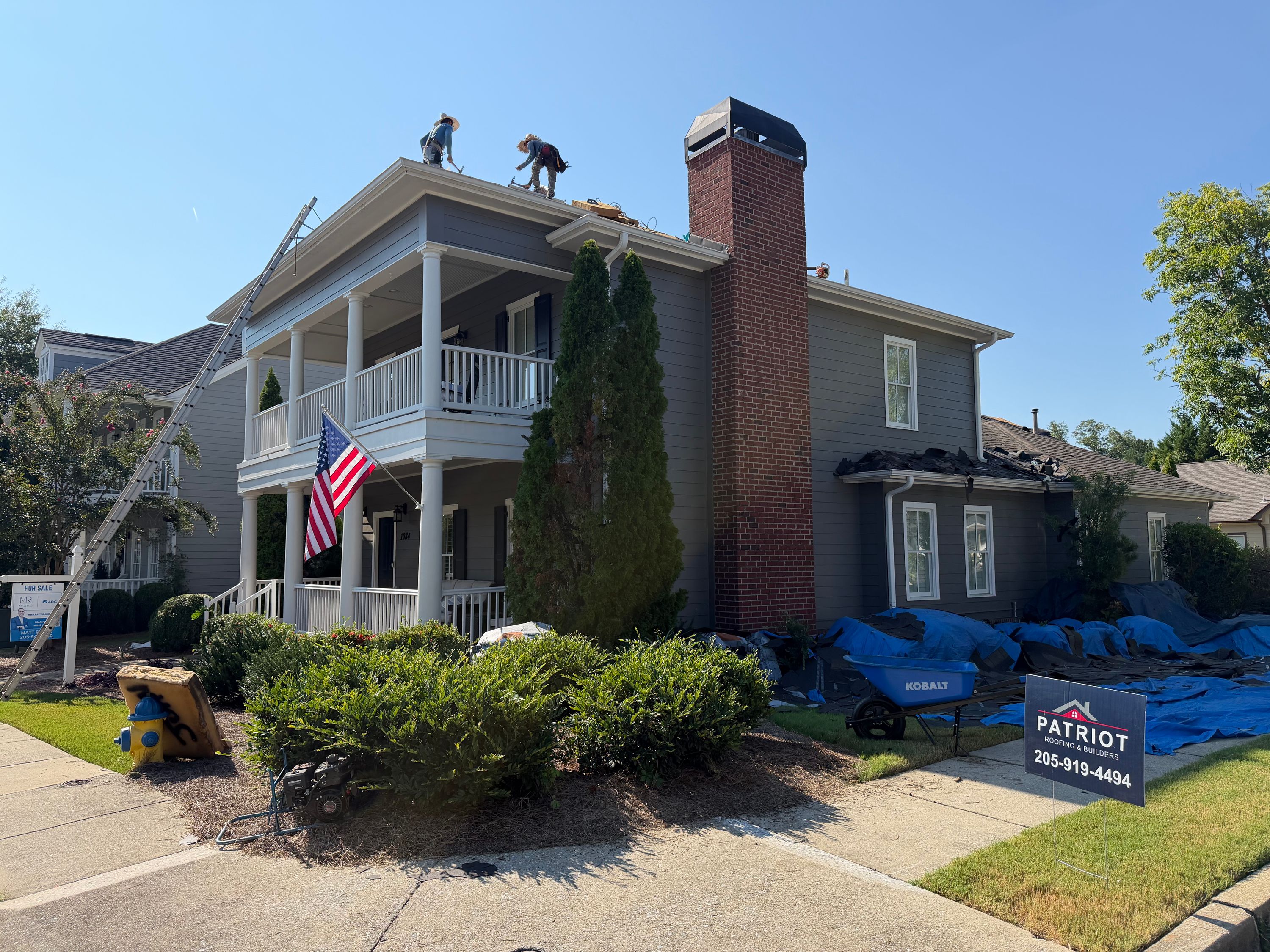 Looking up at a brick chimney and gutter run during an active roof replacement project in Hoover.