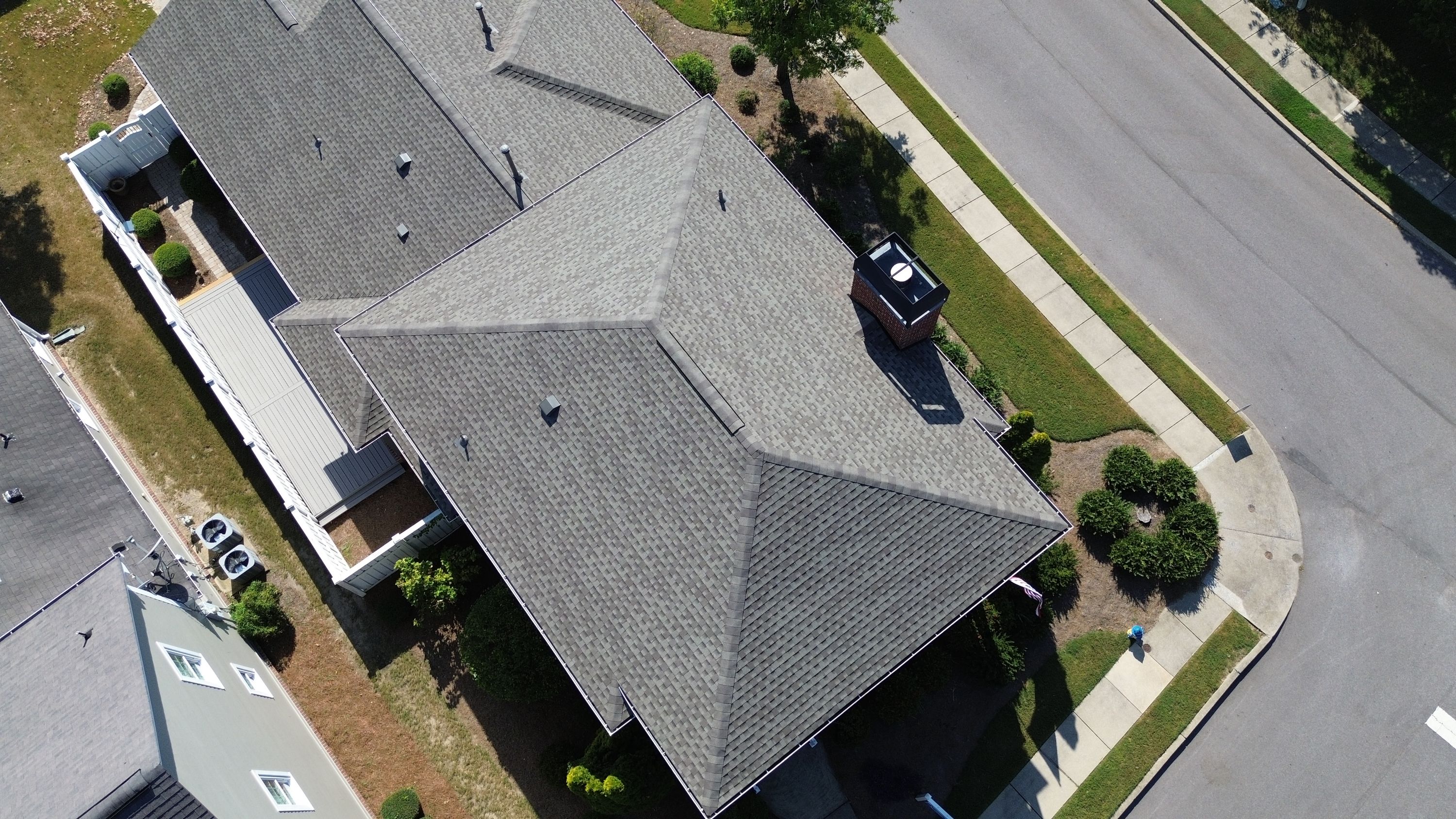 New ridge cap shingles run alongside a brick chimney after a residential roof replacement in the Beaumont neighborhood.