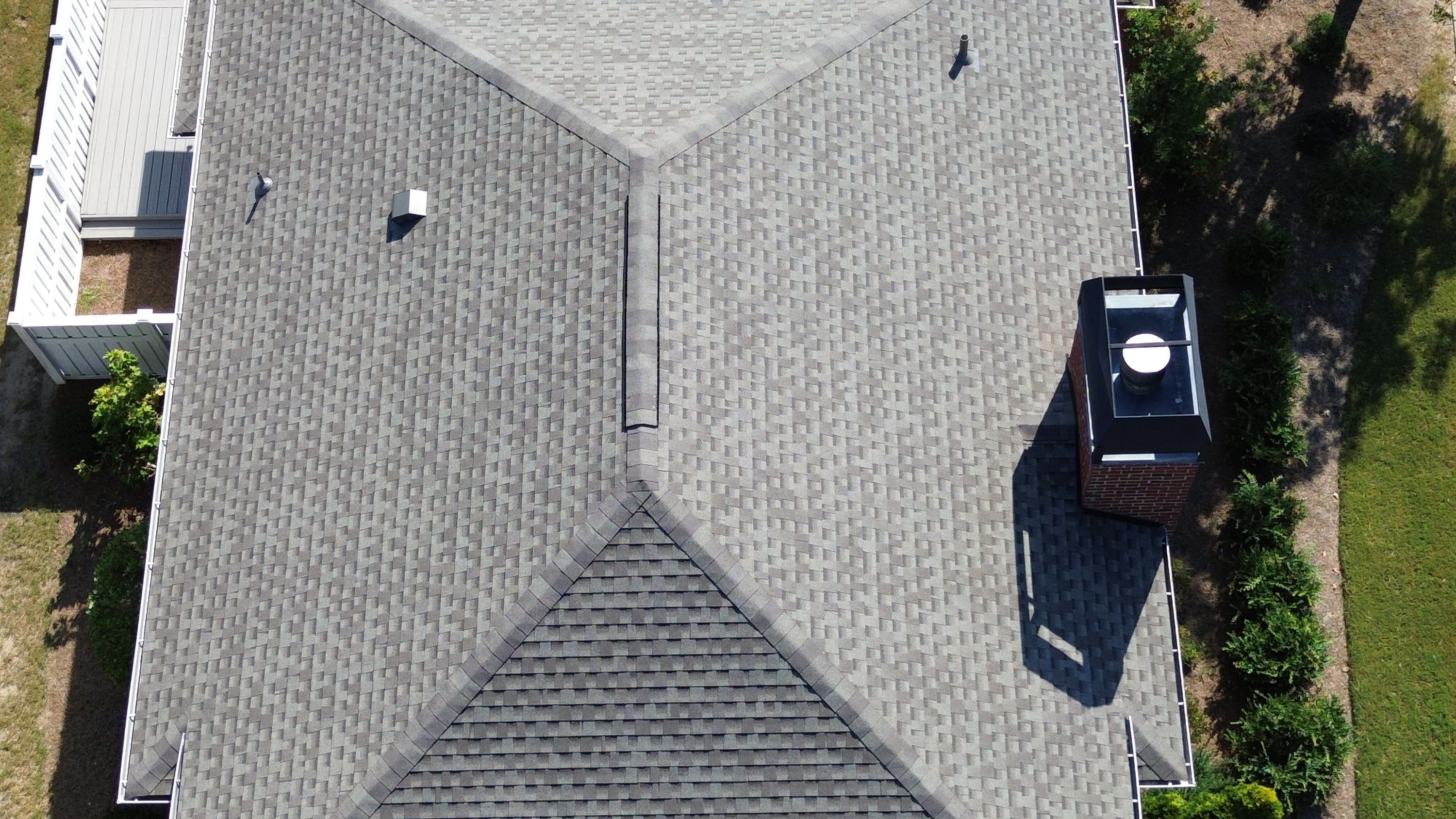 A close-up shot highlights the clean alignment of architectural shingles and ridge capping on the new roof.