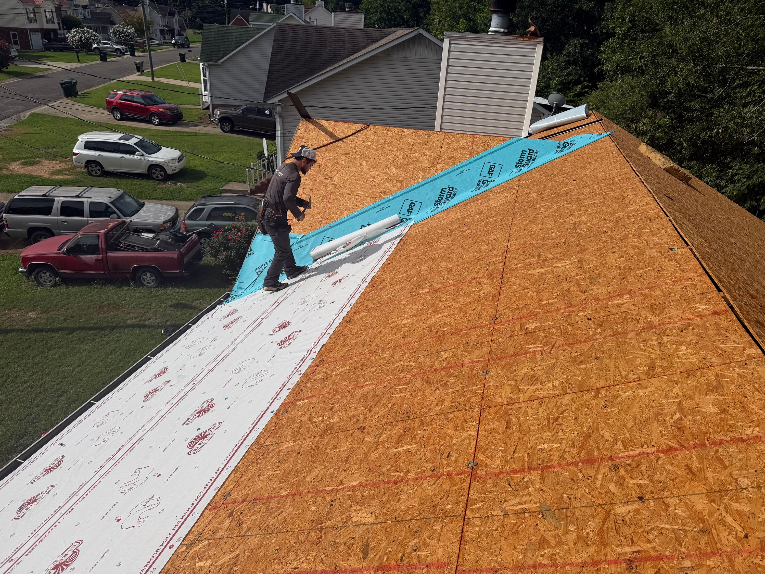 Underlayment and blue GAF StormGuard leak barrier are rolled out onto the new wooden roof decking.