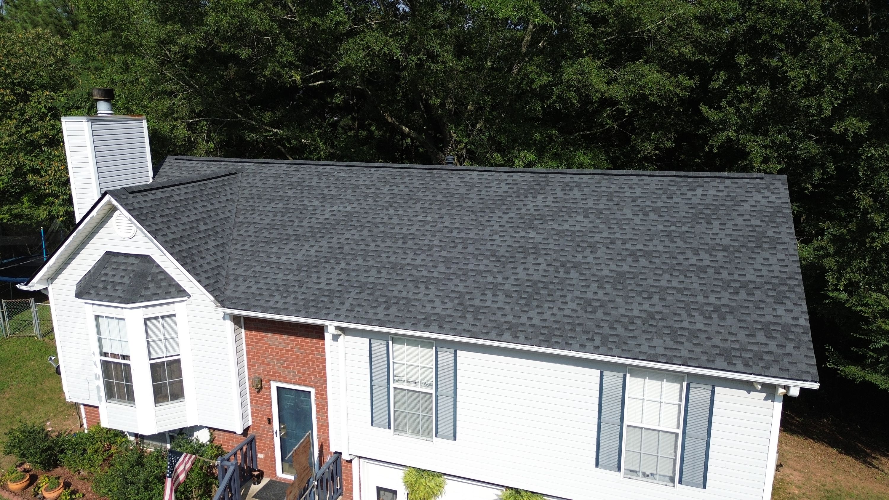 A newly installed gray asphalt shingle roof sits above white siding and blue window shutters.