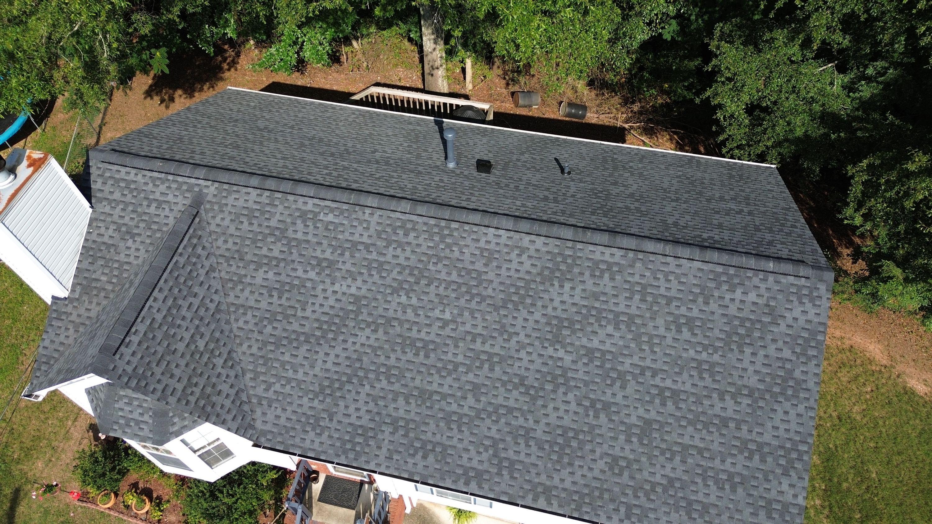 Three new exhaust vents line the upper ridge of a freshly shingled roof plane.