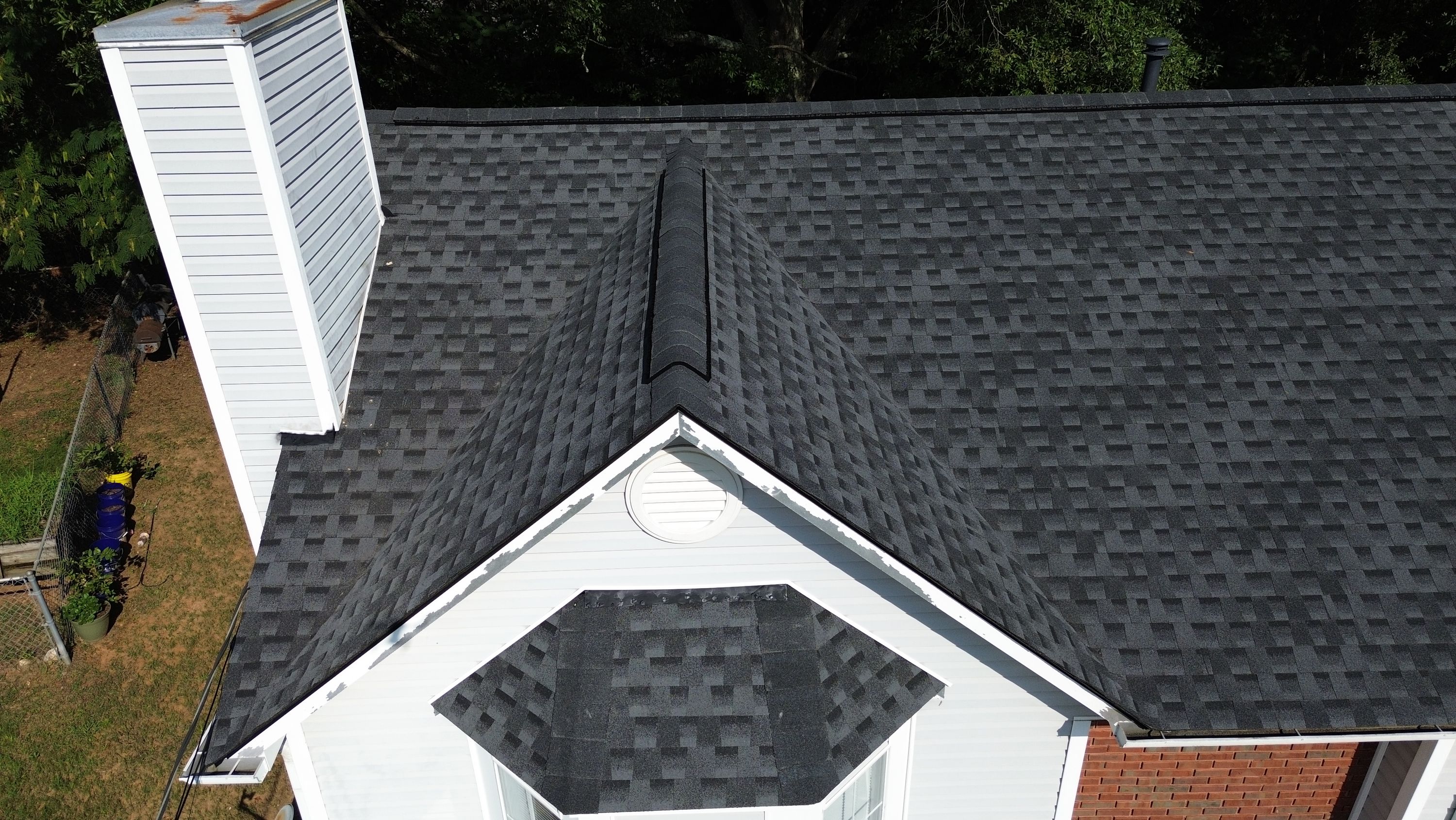 An overhead view shows new dark shingles and a ridge vent above a white circular gable vent in Pebble Lake.