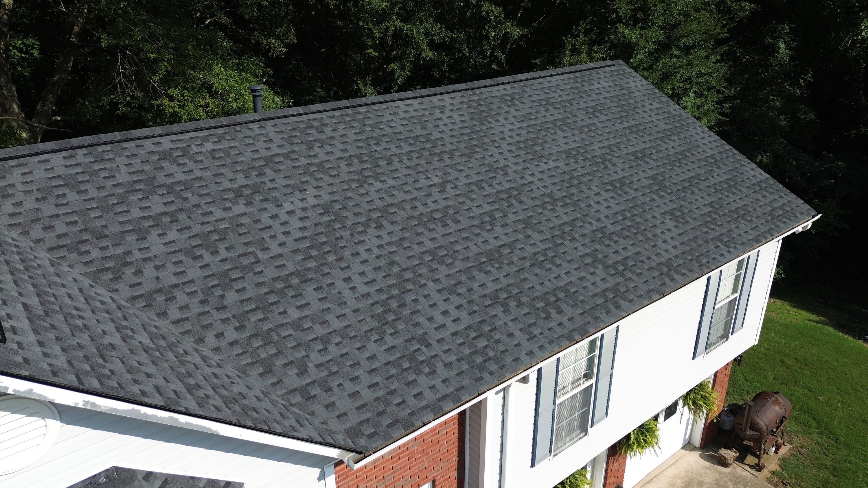 New gray architectural shingles cover a steep roof plane directly above a white gutter and red brick wall.