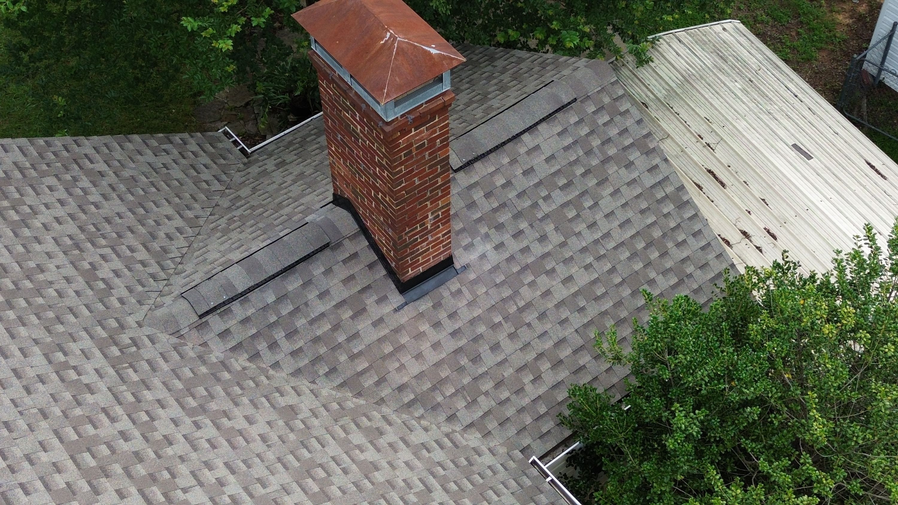 Completed roof replacement with new shingles surrounding a brick chimney for a home in Glen Iris, Birmingham.