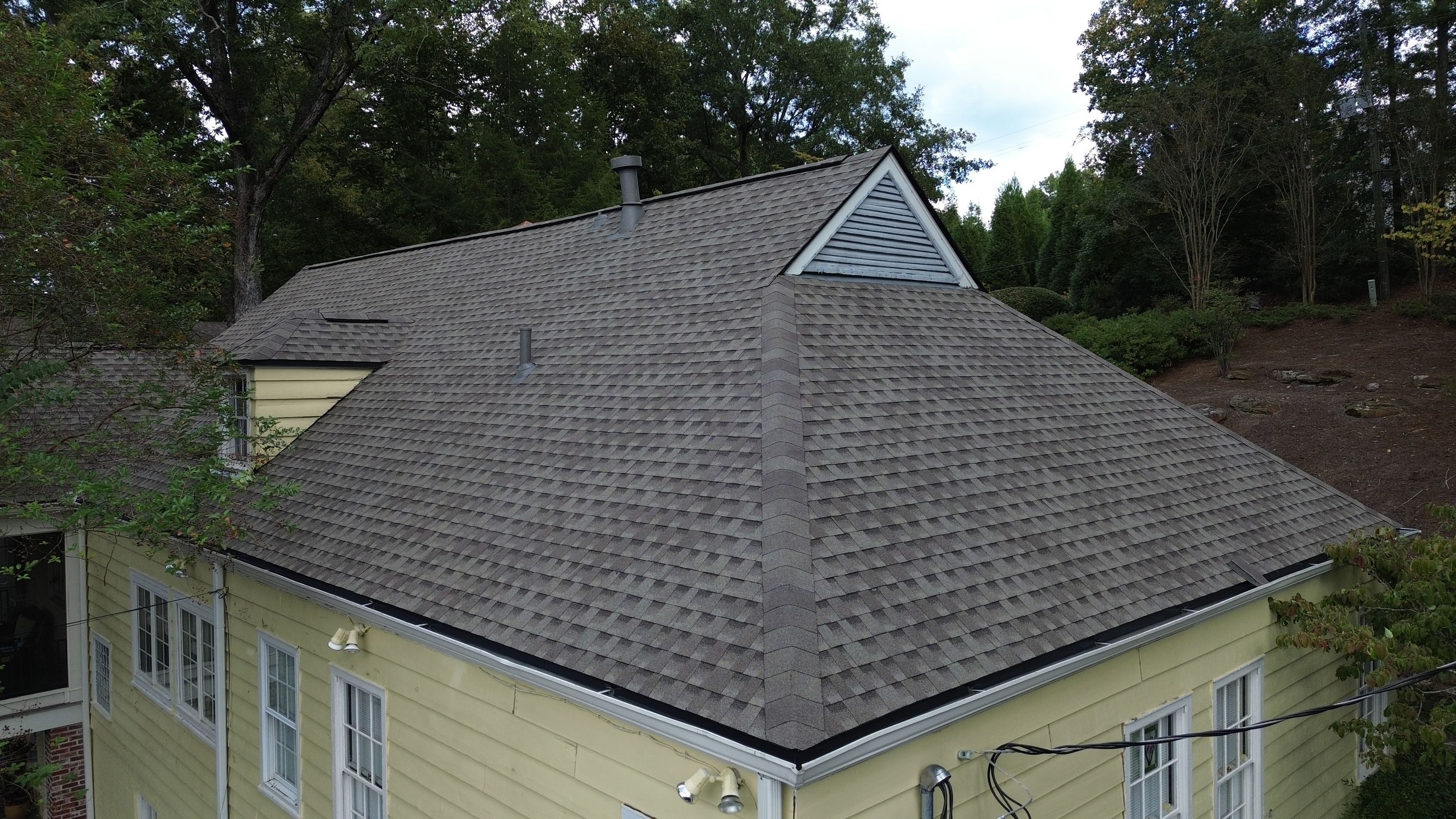 Grey hip cap shingles run down the seam of a newly finished roof replacement.
