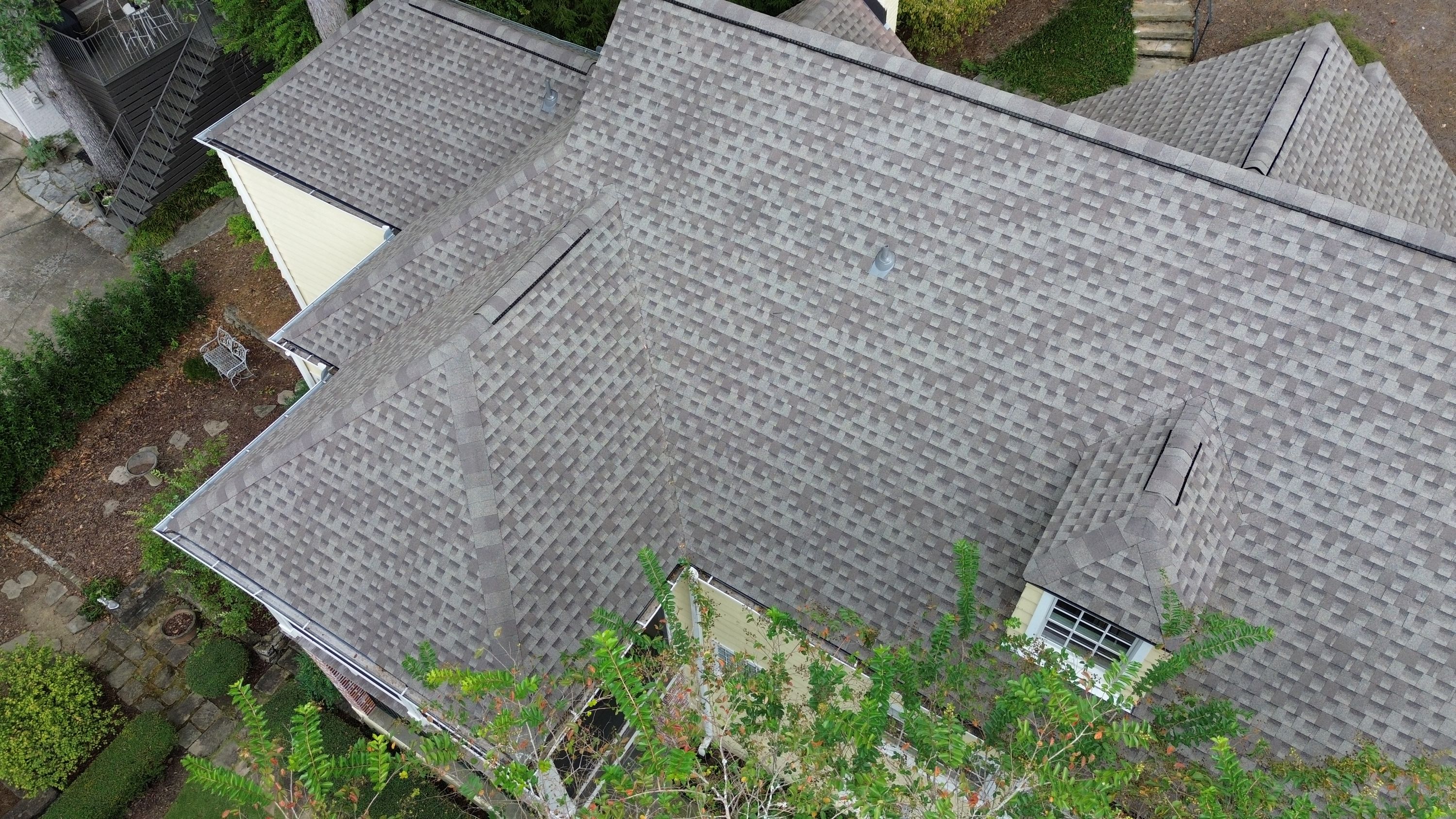 A steep roof valley meets the gutter line of a yellow home, showing newly installed grey shingles.