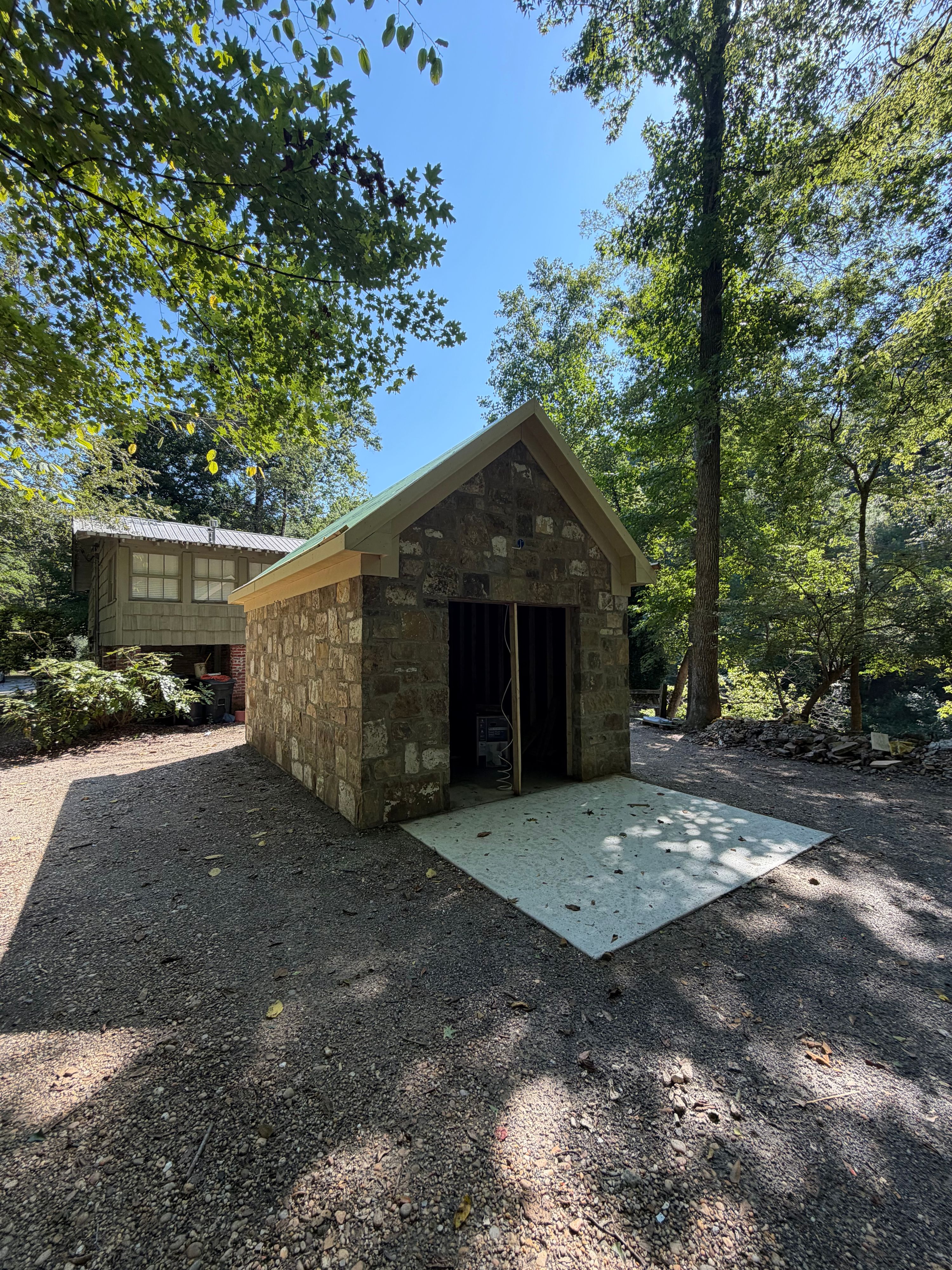 Front gable of a reclaimed stone corn shed under construction on the Cahaba River in Vestavia Hills, AL, with framed doorway and concrete apron