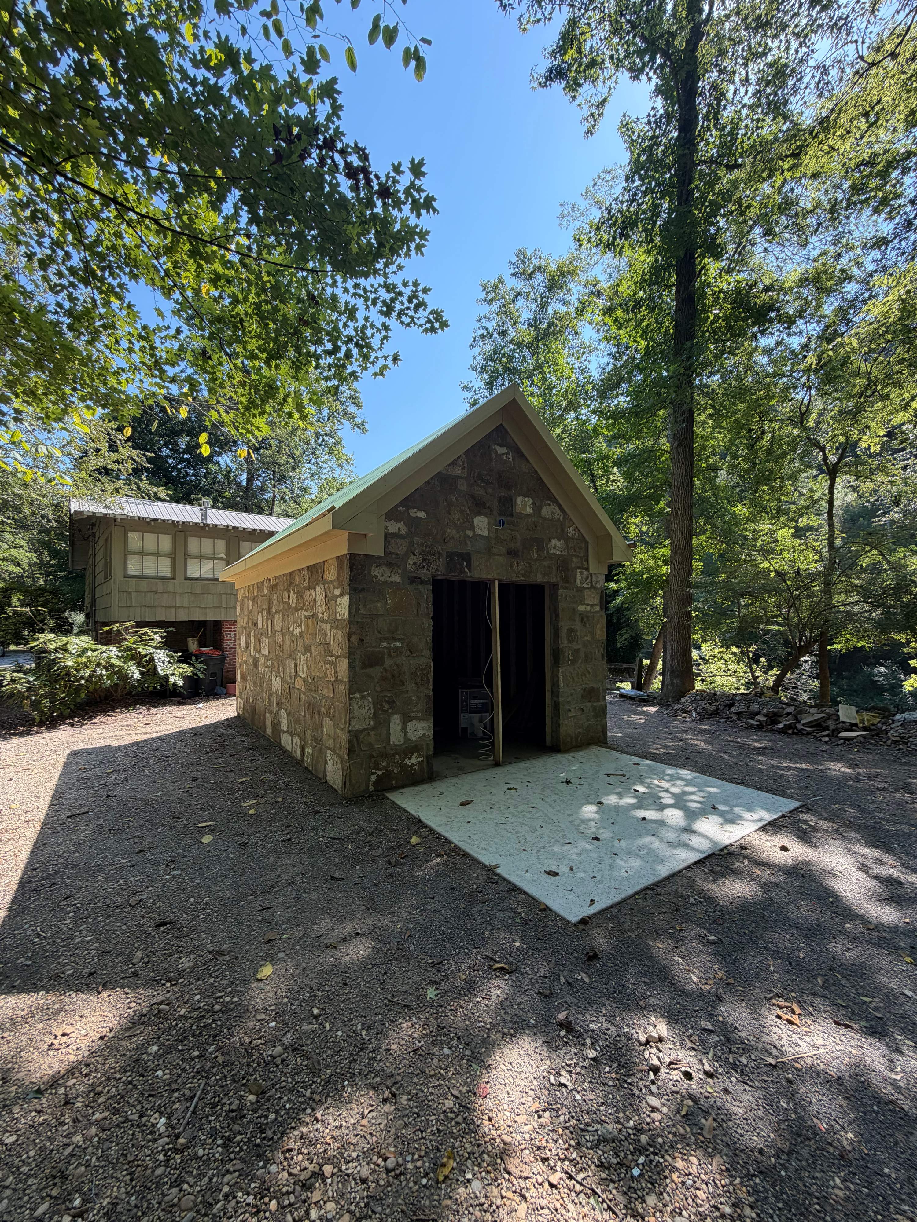 Front gable of a reclaimed stone corn shed under construction on the Cahaba River in Vestavia Hills, AL, with framed doorway and concrete apron