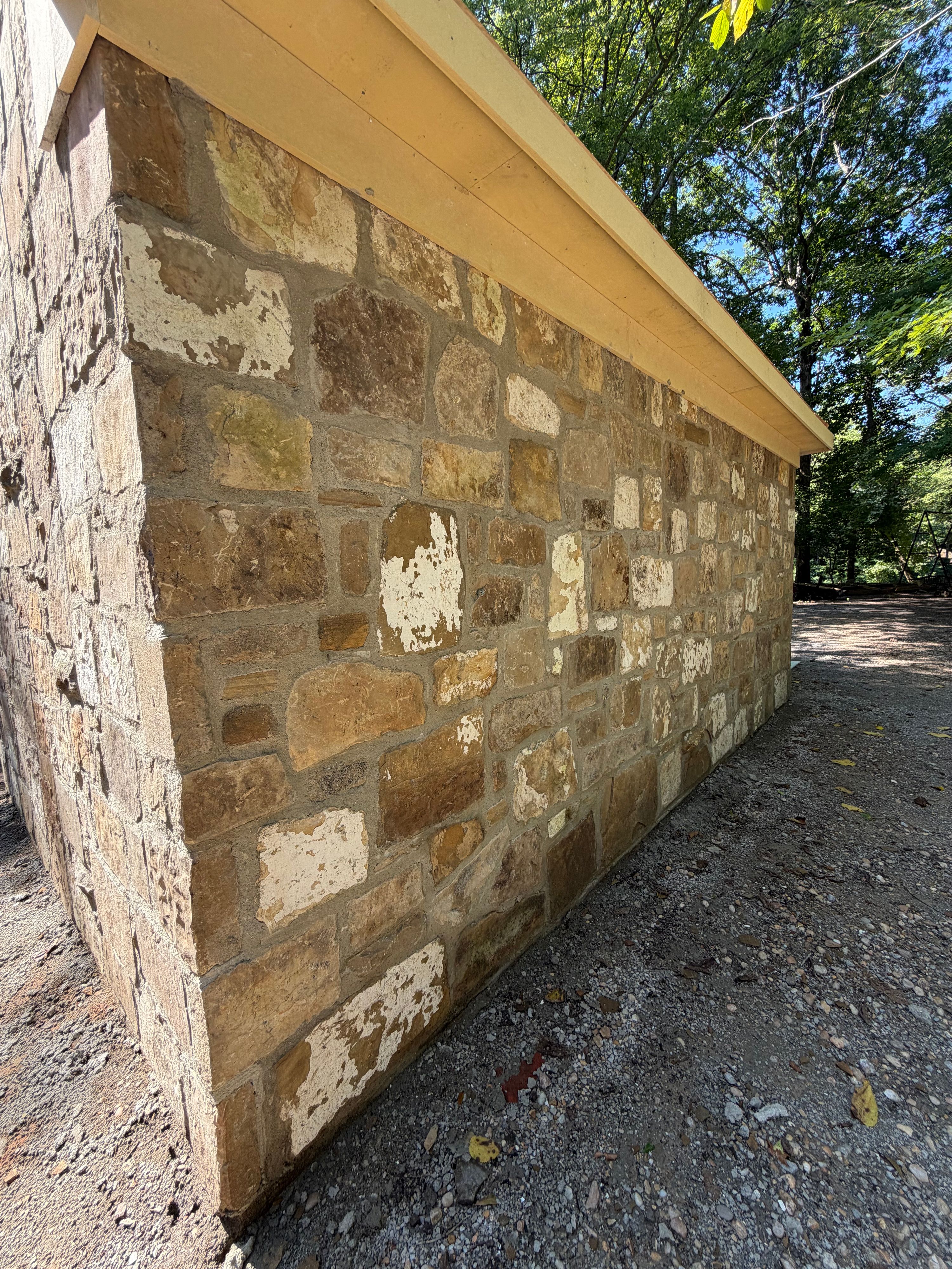 Long masonry wall of salvaged stone showing white paint remnants and weathered patina