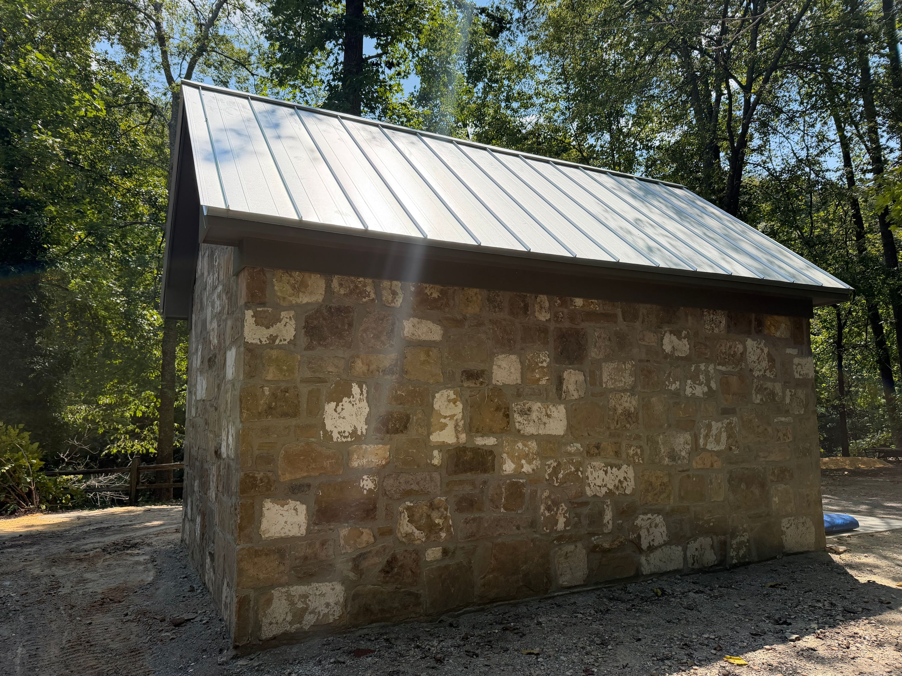 Newly installed metal roofing panels meet a dark drip edge above a reclaimed stone wall.