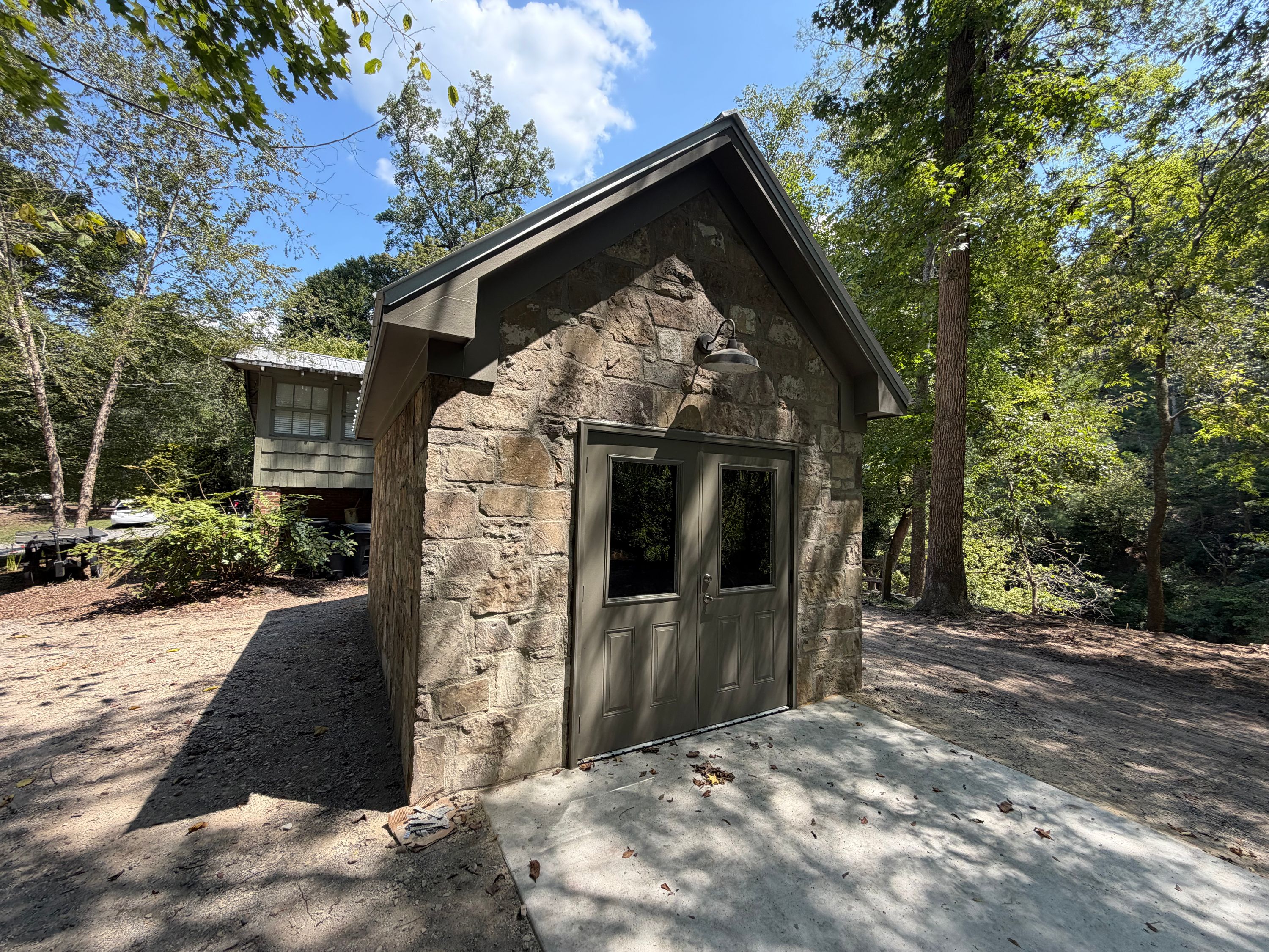 Sunlight highlights a gray double door and gooseneck light fixture on the rustic stone facade.