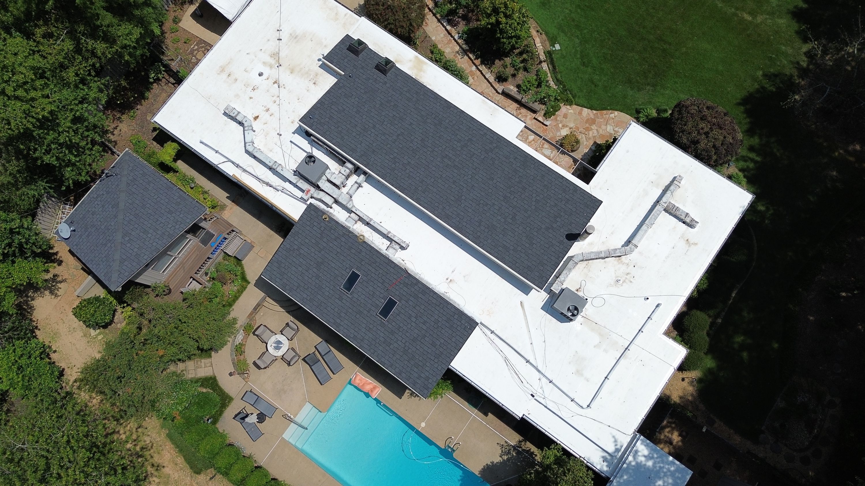 White flat roofing membranes run alongside newly installed dark shingles near a swimming pool.