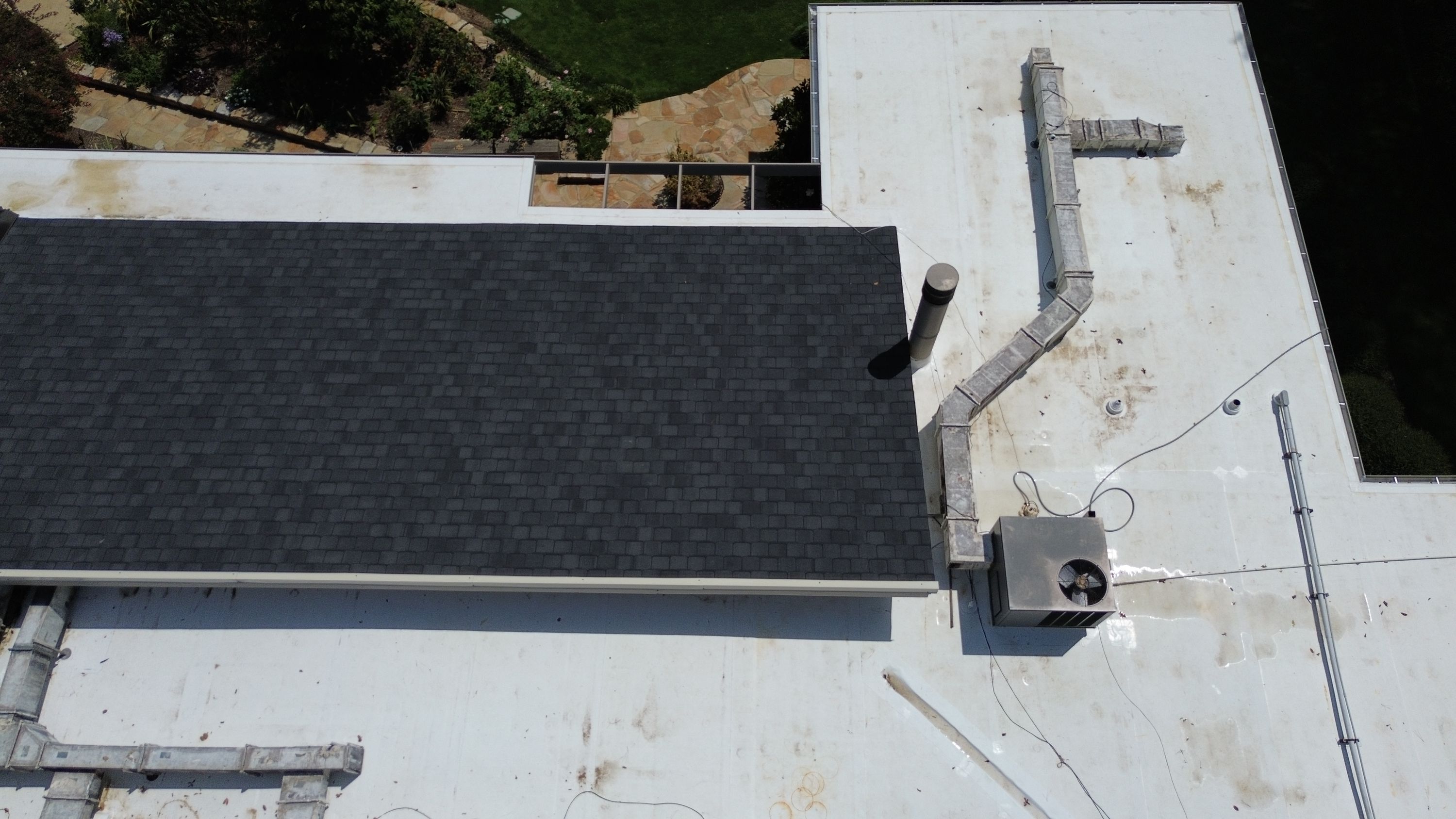 Freshly installed dark shingles form a neat rectangular section bordered by white flat roofing.