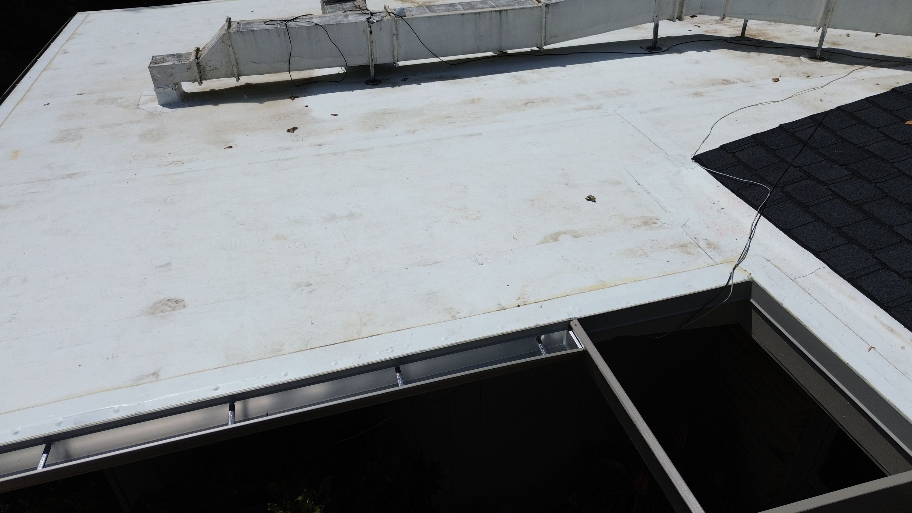 Close-up of a newly installed metal gutter run along the edge of a white flat roof membrane.