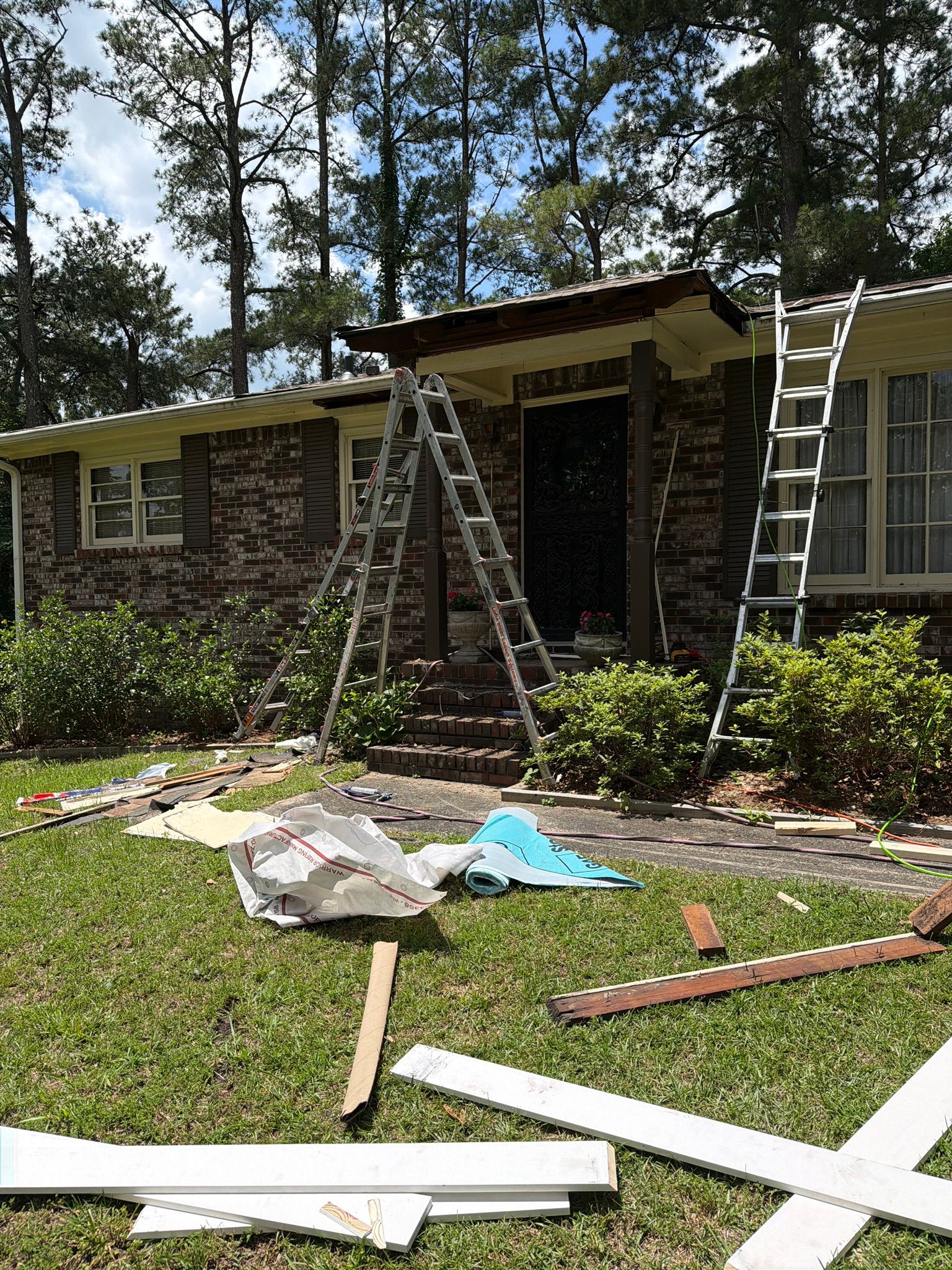 Ladders stand on a Leeds lawn during front porch roof and trim repairs on a brick ranch house.