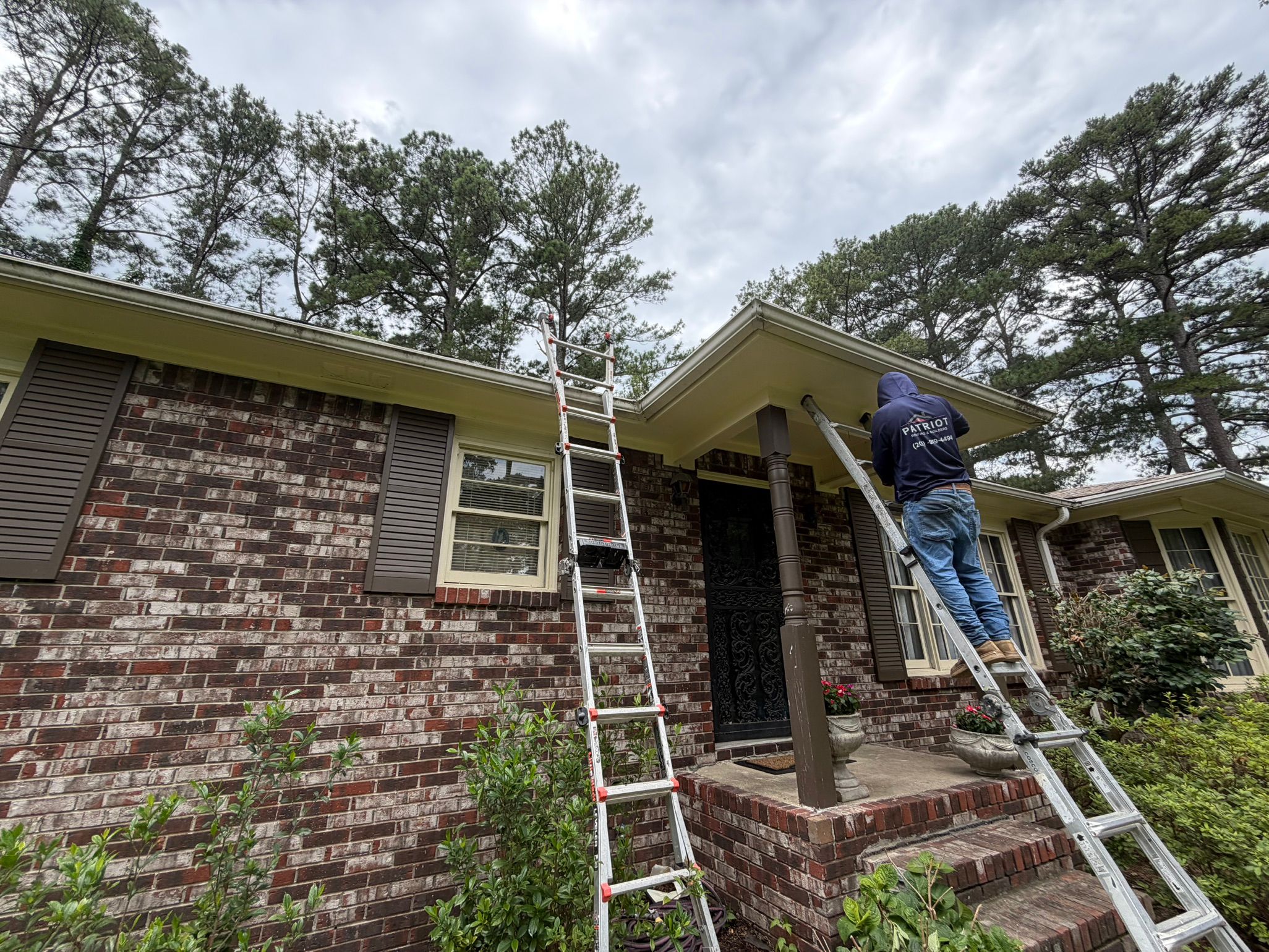 An extension ladder rests against the newly repaired white gutter system of a brick home.